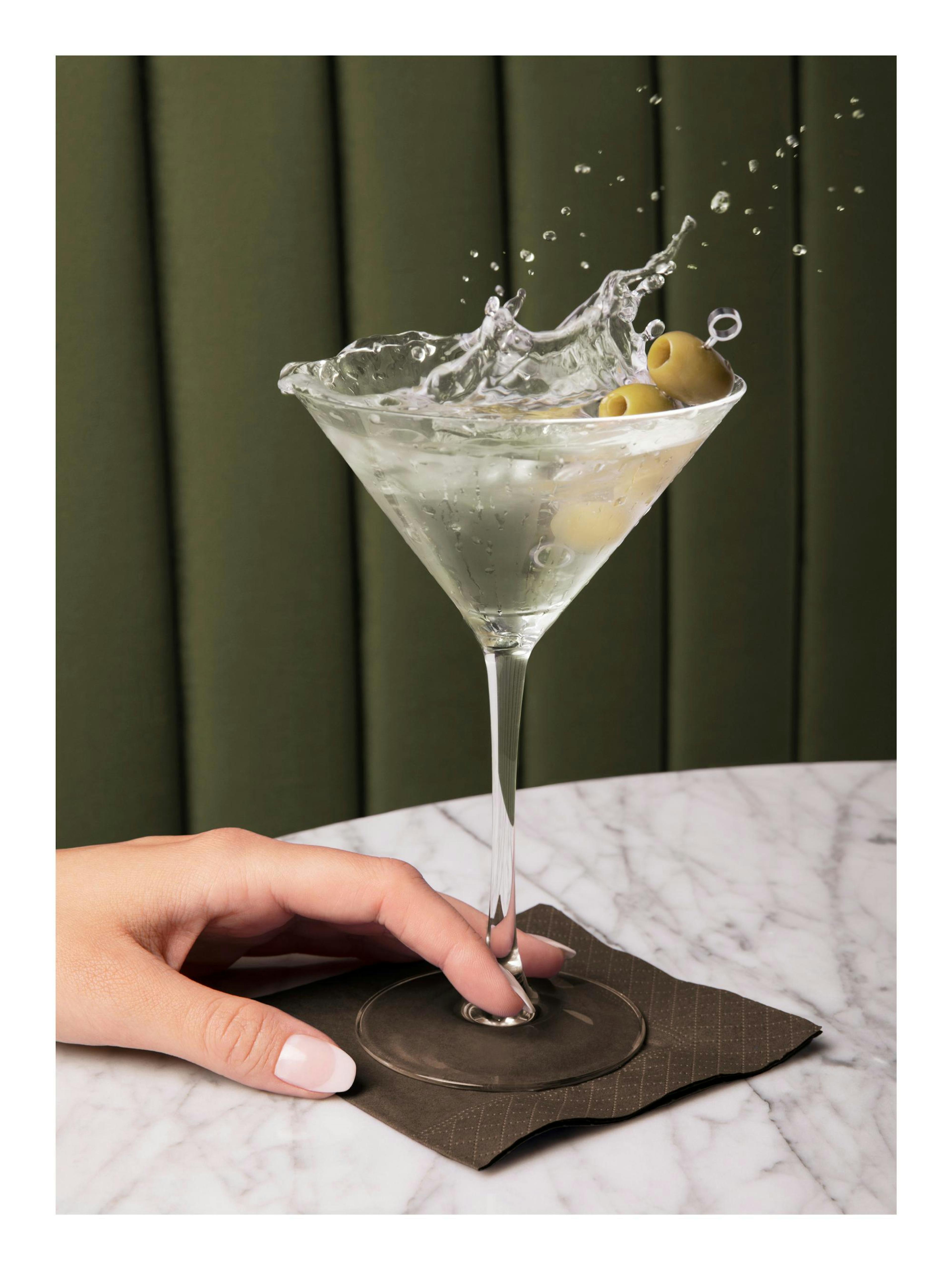 Póster de martini seco con aceitunas verdes. Salpicadura de bebida clásica en copa.