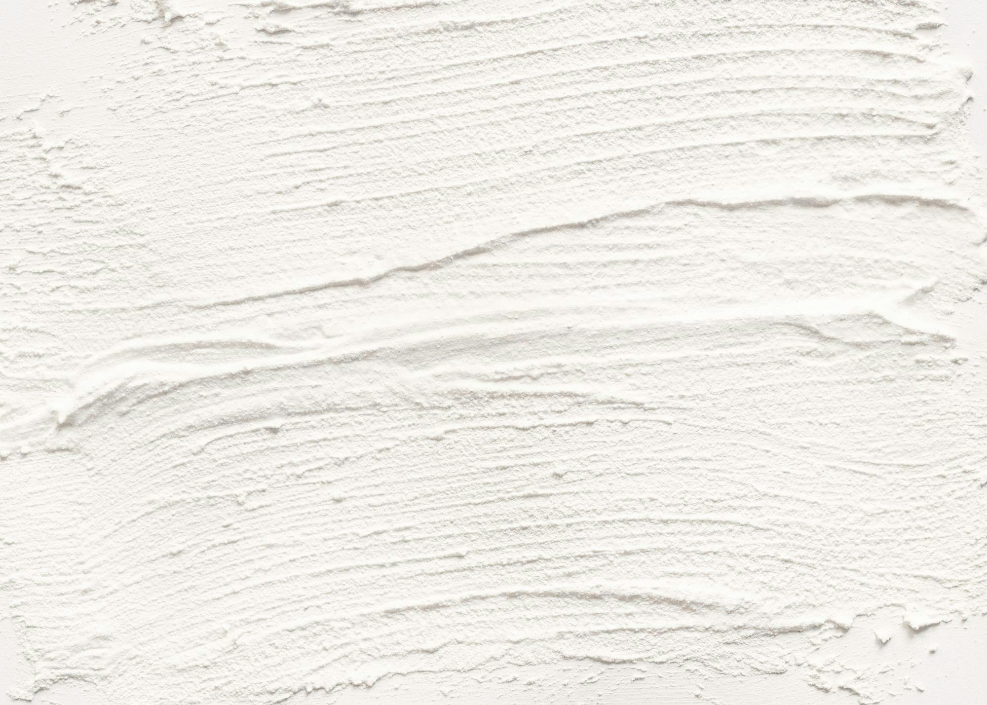 En texturerad vit poster som liknar grov puts hänger i ett minimalistiskt vardagsrum ovanför en beige soffa.