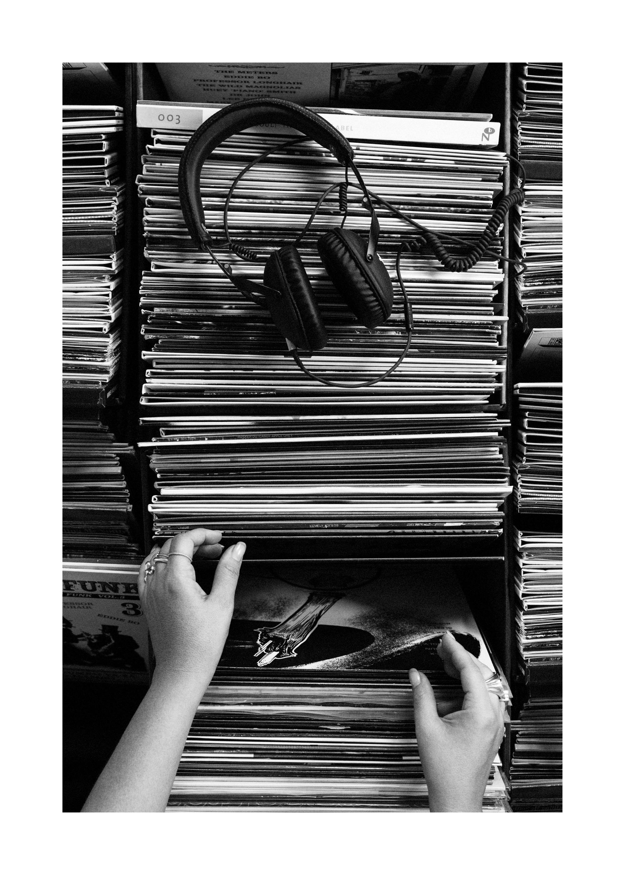 Affiche monochrome dune femme cherchant un disque vinyle dans une archive, avec un casque posé sur des disques, musique nostalgi