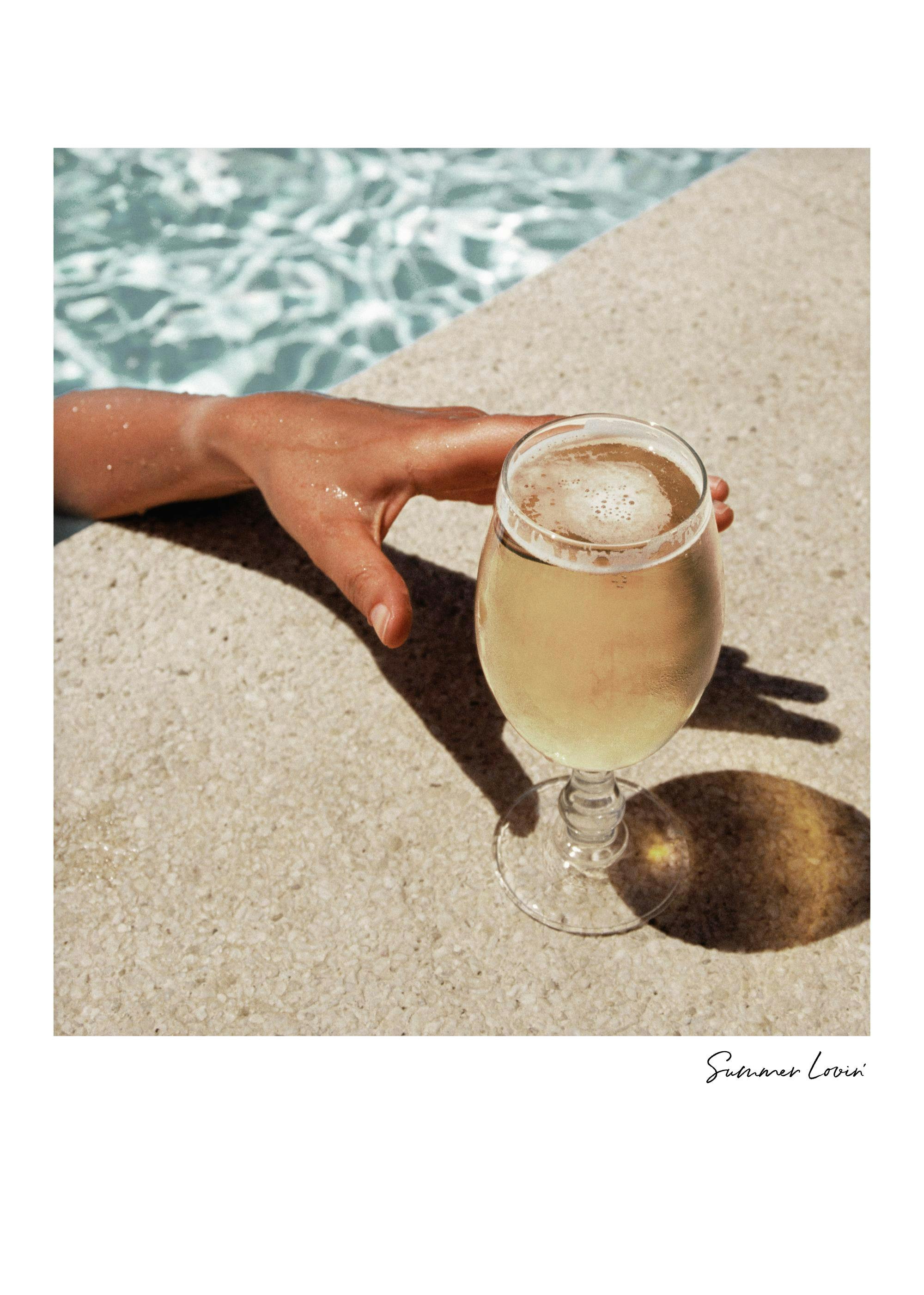 Summer Lovin poster: Hand reaching from pool to drink, sun-kissed skin, refreshing summer beverage, vibrant photo art.