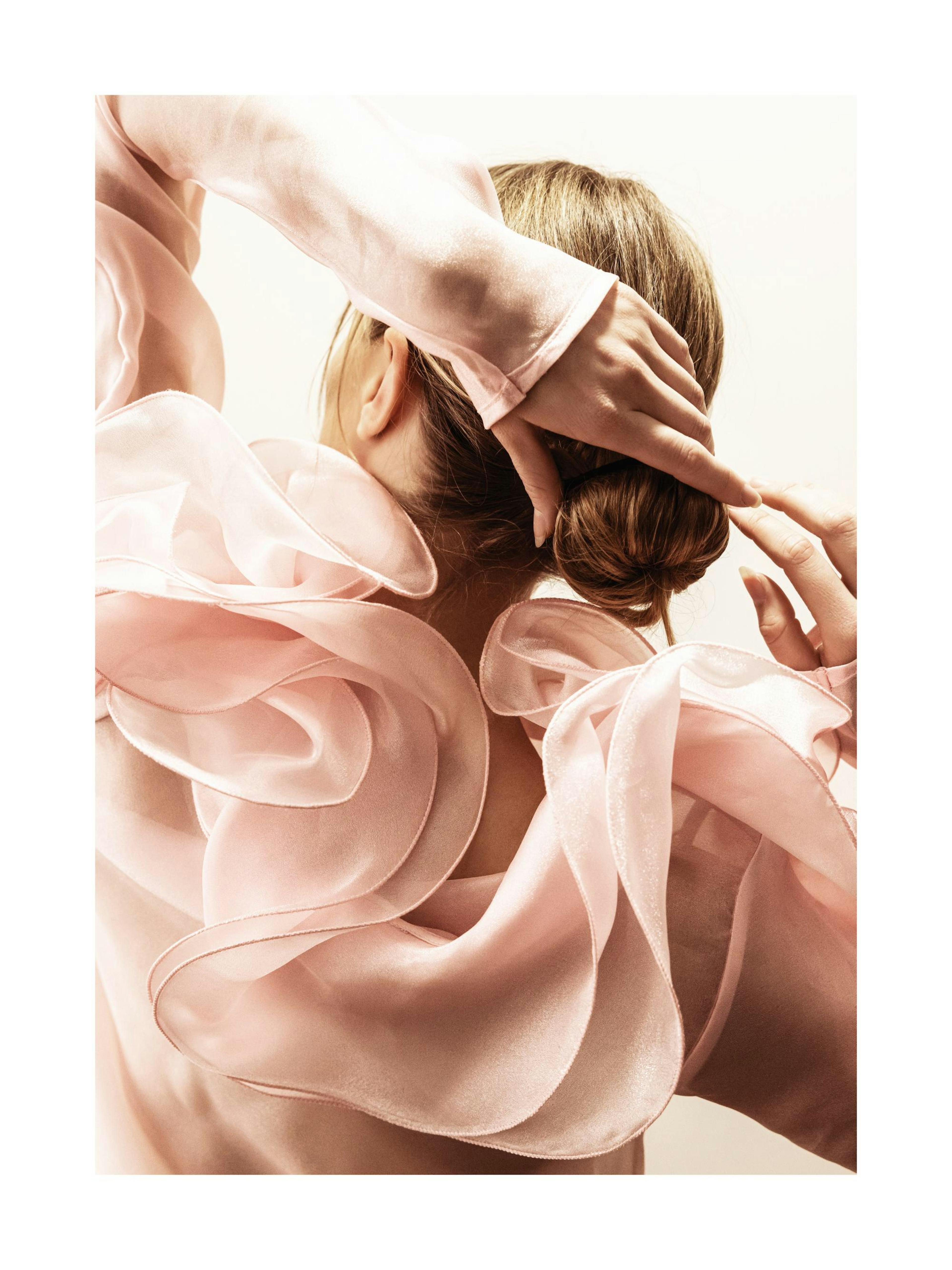 Ballerina in pink dress from behind with hands behind her head, hair in a bun. Ballet photography.