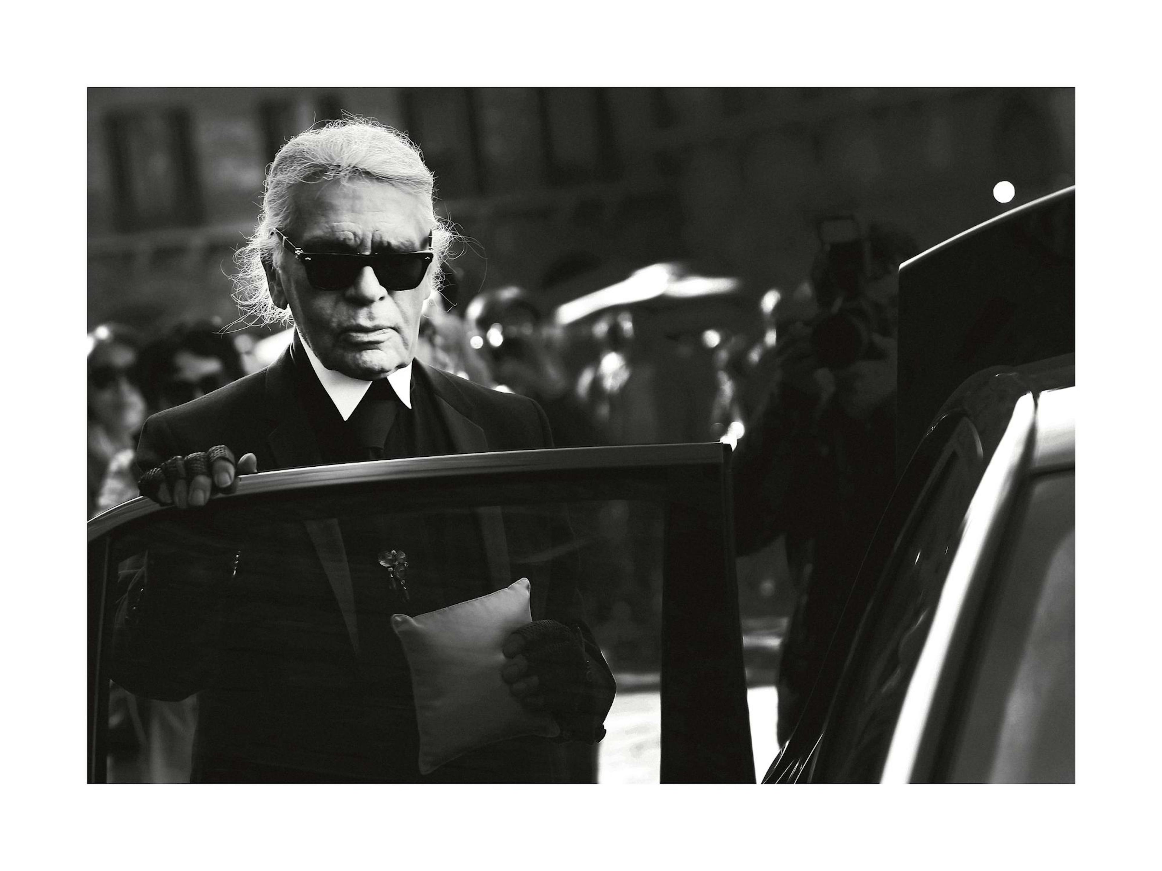 Fotografia in bianco e nero dello stilista Karl Lagerfeld che esce da unauto. Iconico poster di moda.
