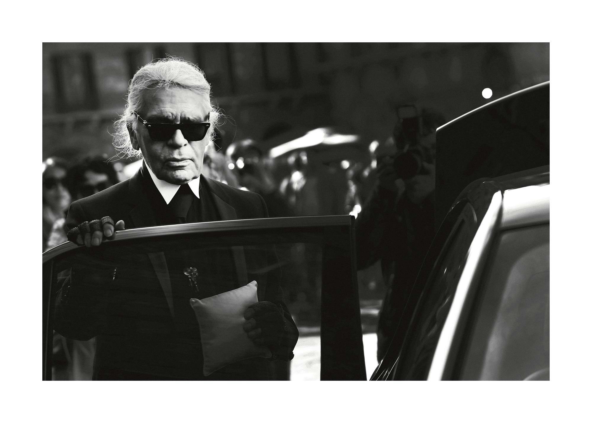 Schwarz-Weiß-Fotografie von Karl Lagerfeld mit Sonnenbrille und Handschuhen, der aus einem Auto steigt. Ikonischer Modedesigner,