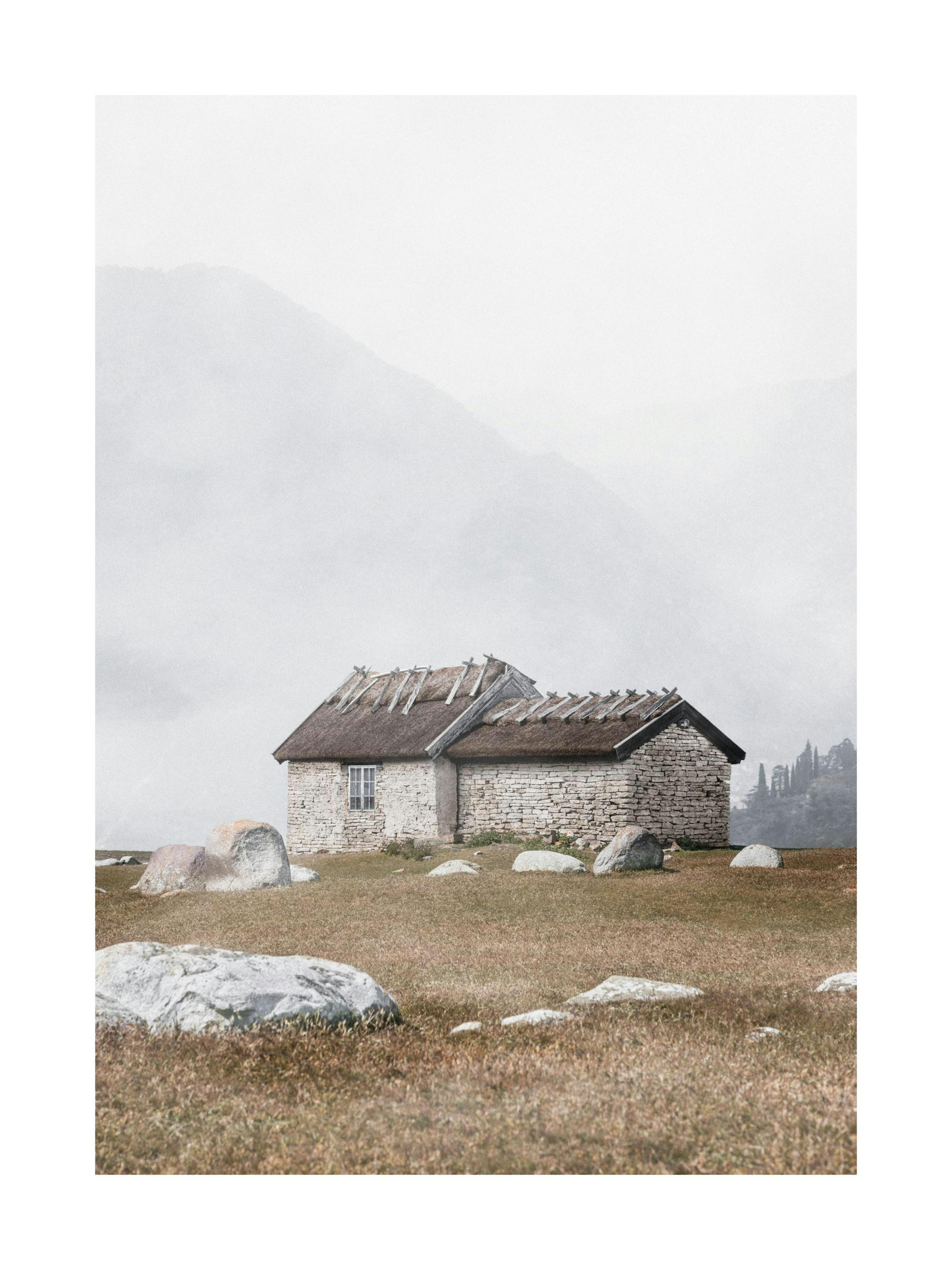 Póster de una cabaña de piedra con tejado de paja en una ladera rocosa, en un día nublado, exhibido en una sala moderna.