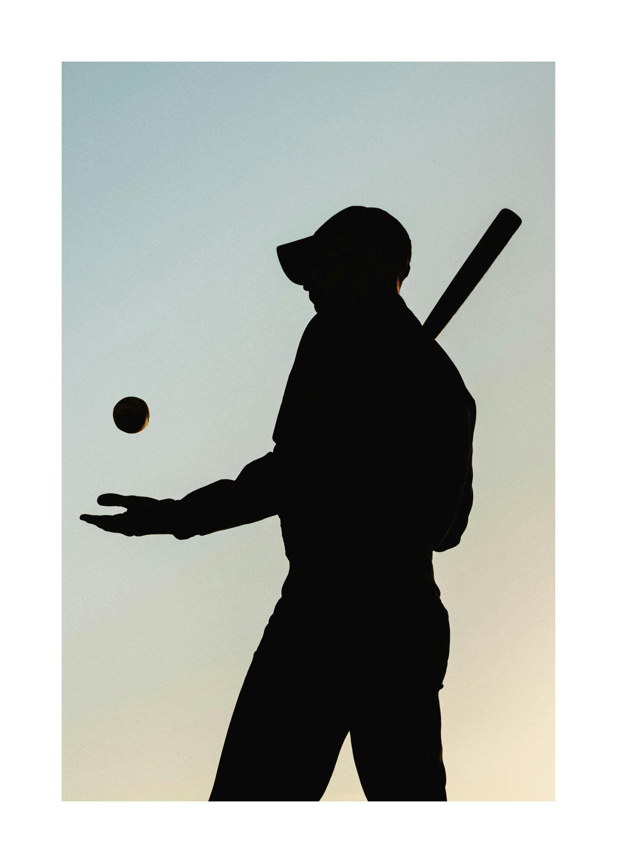 Baseball player silhouette in black, holding a bat, with a baseball hovering above an open palm against a gradient sky.