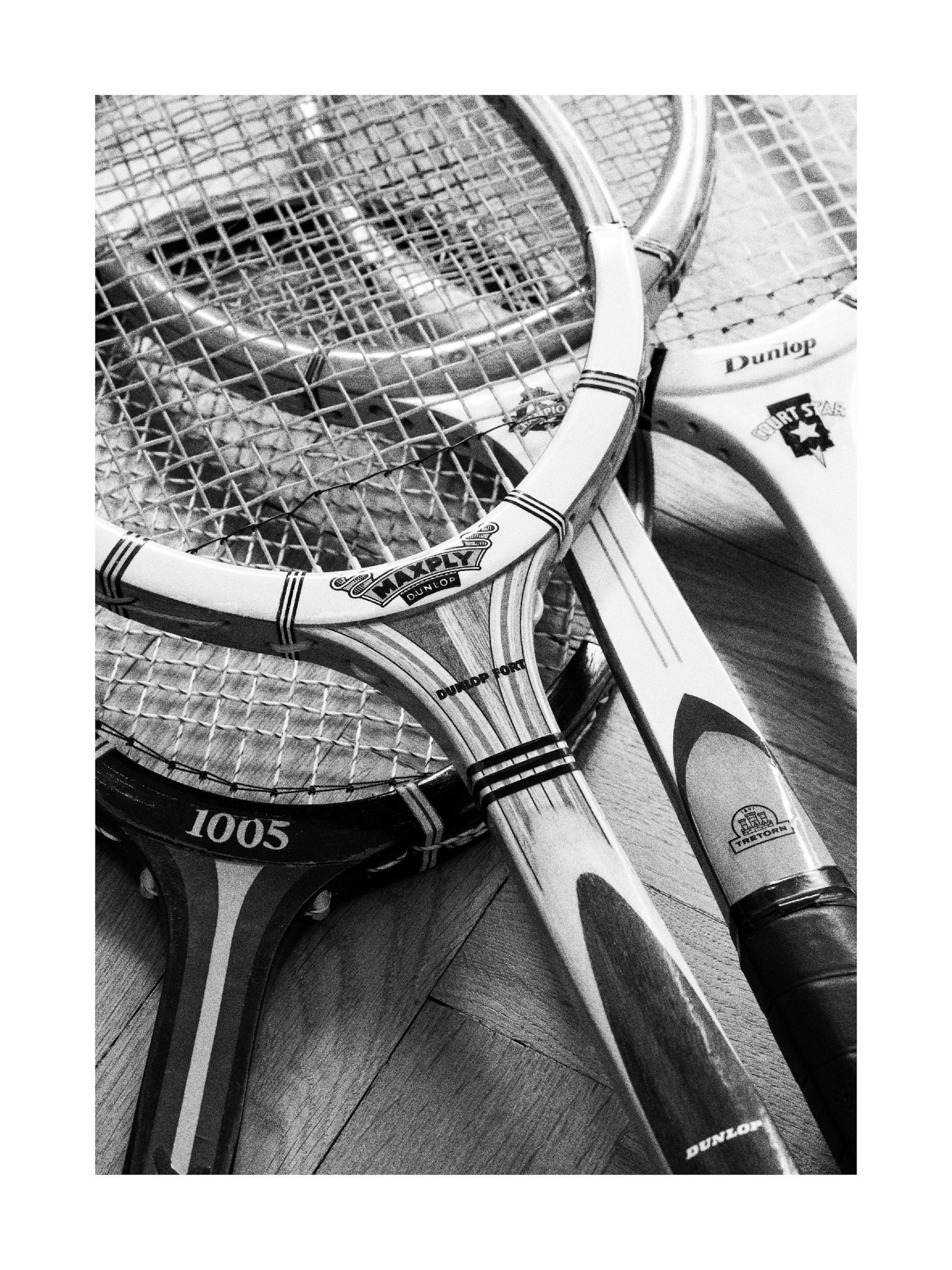 Schwarz-Weiß-Fotografie von drei Vintage-Tennisschlägern auf Holzboden