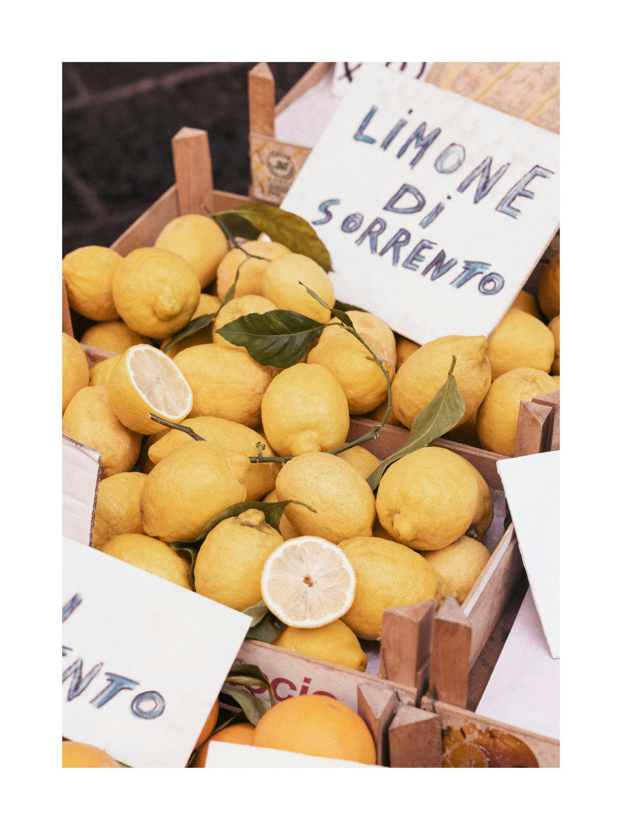 En trälåda fylld med Sorrento-citroner, en del hela och en del delade, med gröna blad och en handskriven skylt LIMONE DI SORRENT