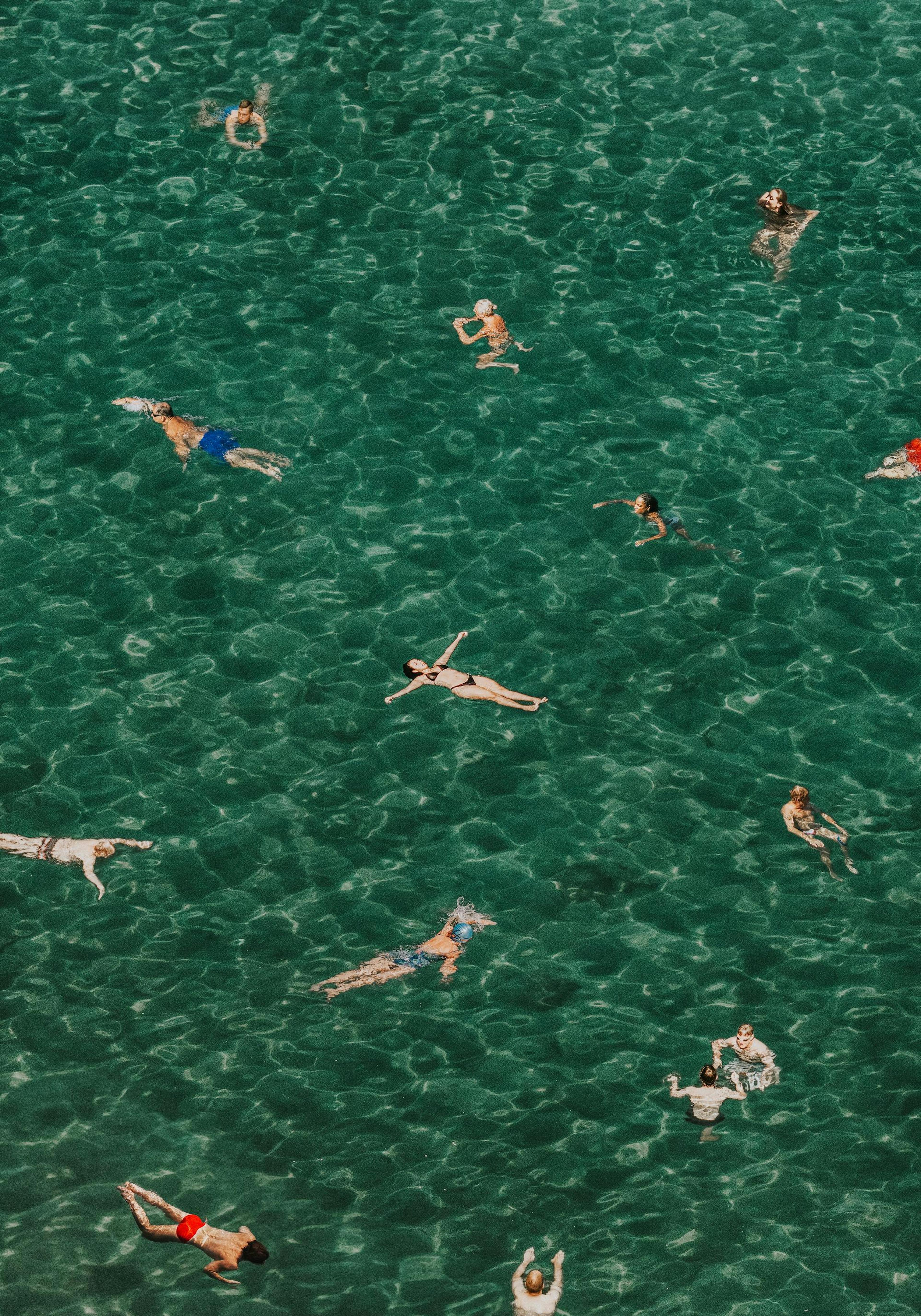 Overhead view of swimmers floating in clear, calm Italian ocean water, a serene Mediterranean scene poster.