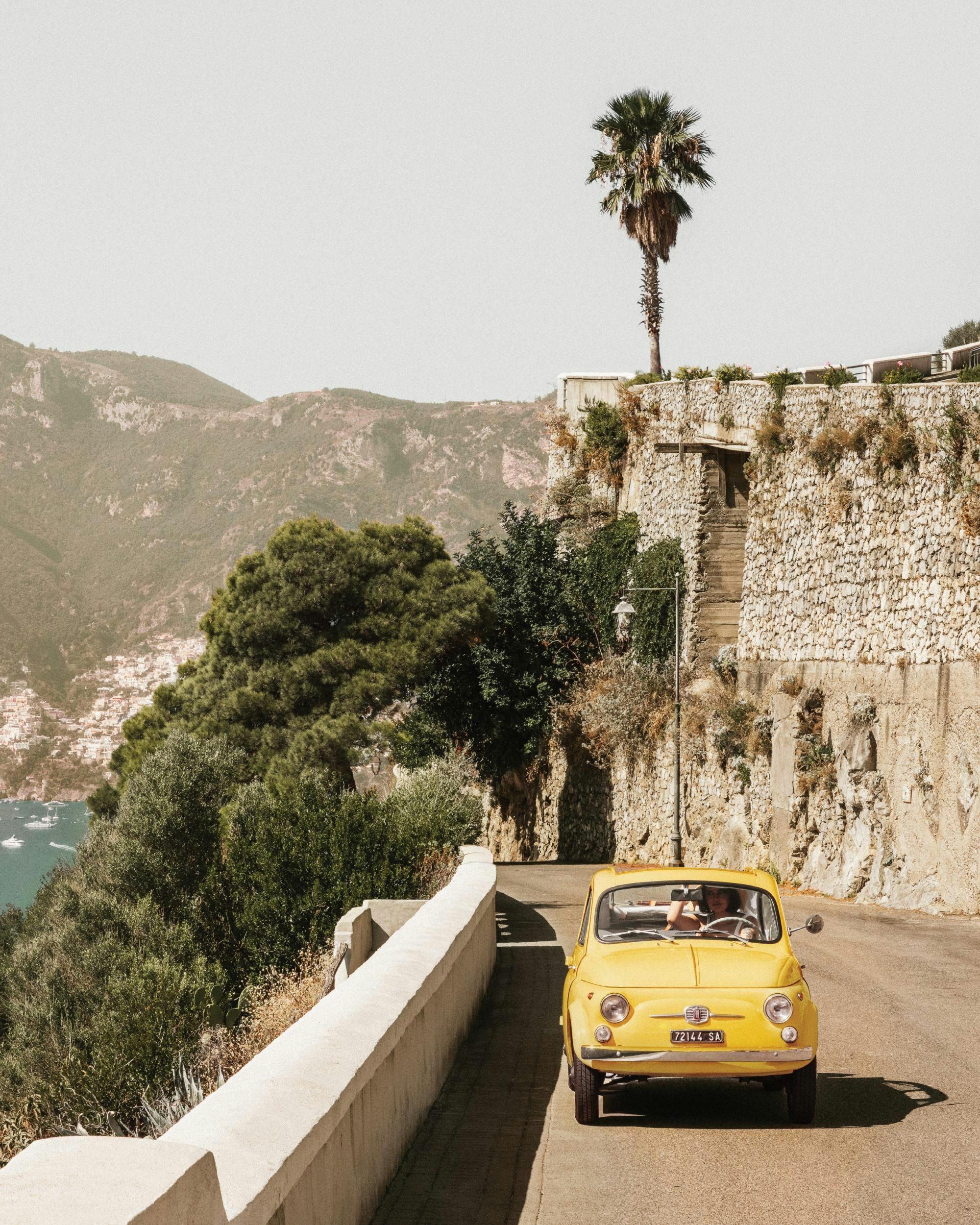 Gul bil på Amalfikusten, Italien. Kustväg med palmer, berg och hav i bakgrunden.