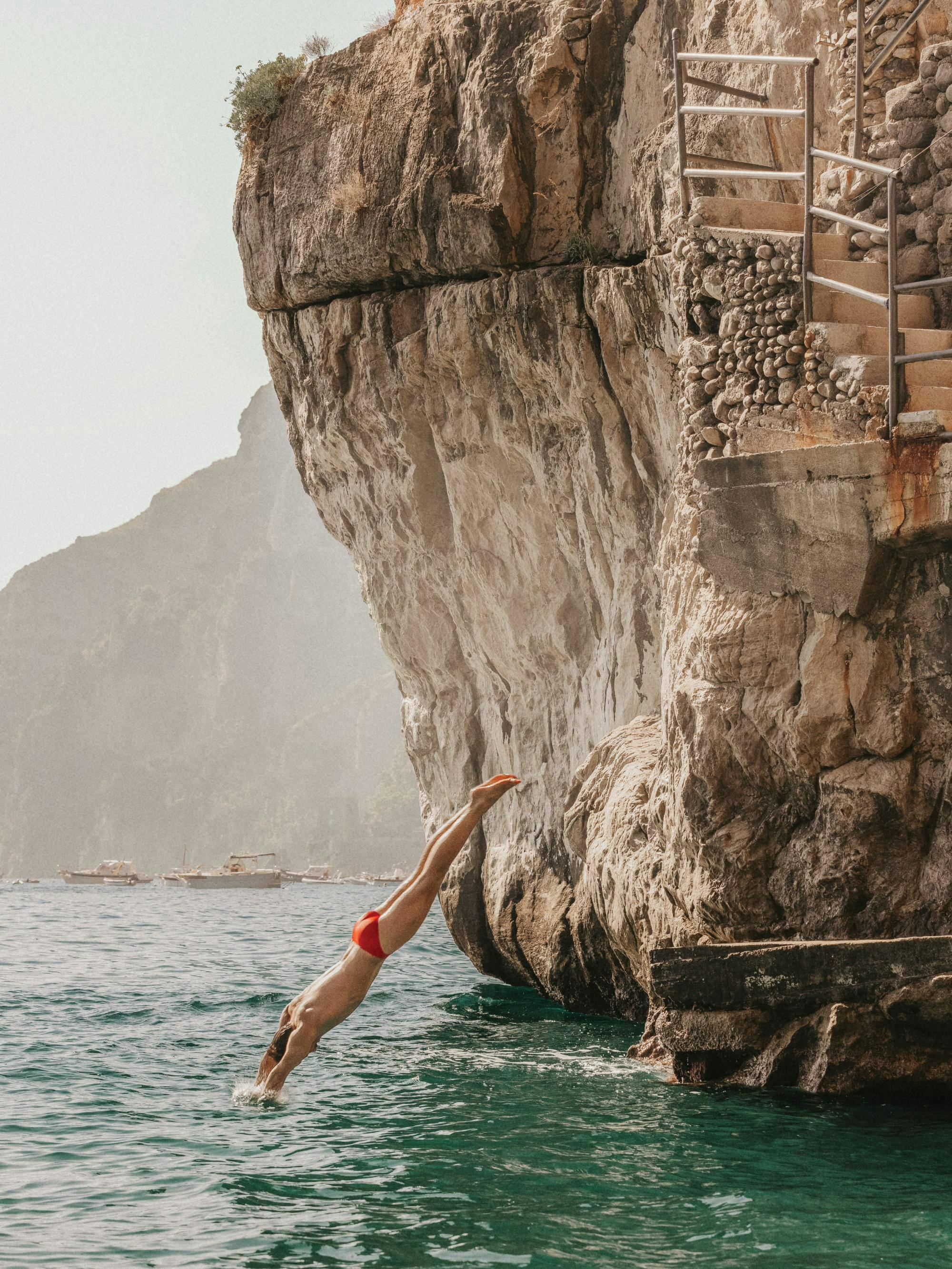 Affiche dun homme en maillot de bain rouge plongeant dans locéan depuis une falaise rocheuse, avec effet granuleux.