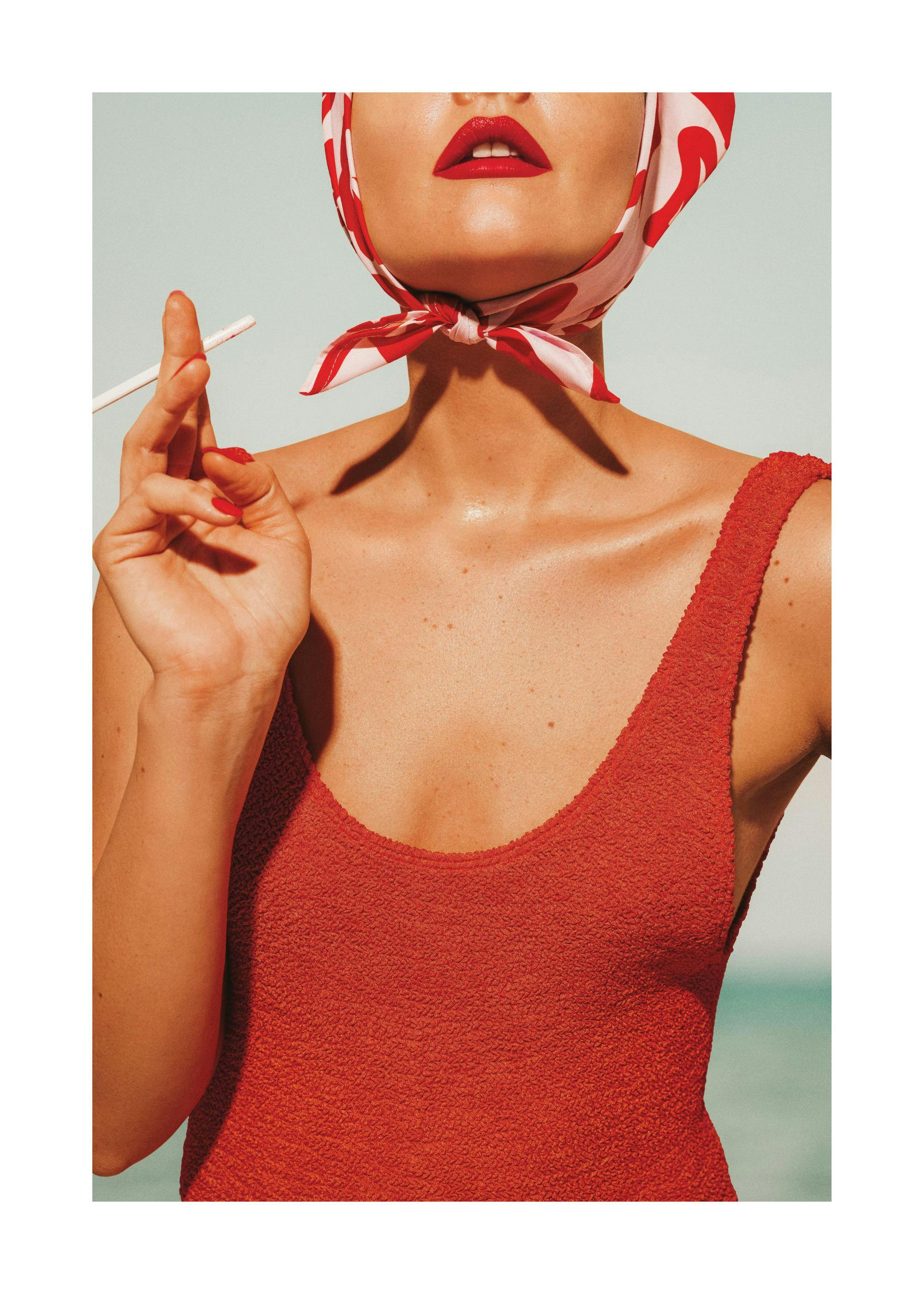 Affiche Bella Donna: femme en maillot de bain rouge avec foulard et lèvres rouges, tenant une cigarette, sur fond bleu doux.