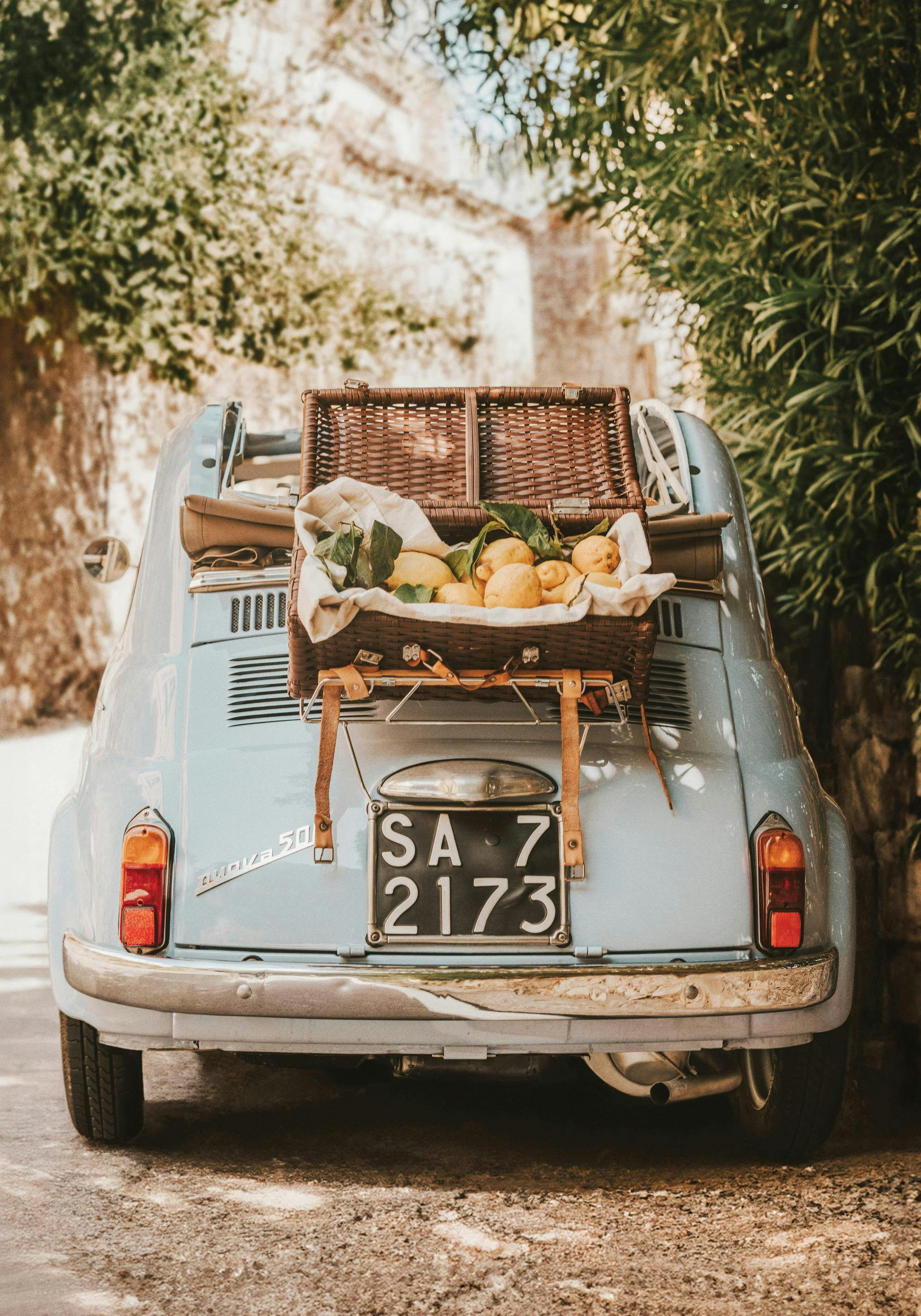 Póster de un coche antiguo azul claro con cesta de picnic y limones, estilo retro italiano, nostalgia de viaje.