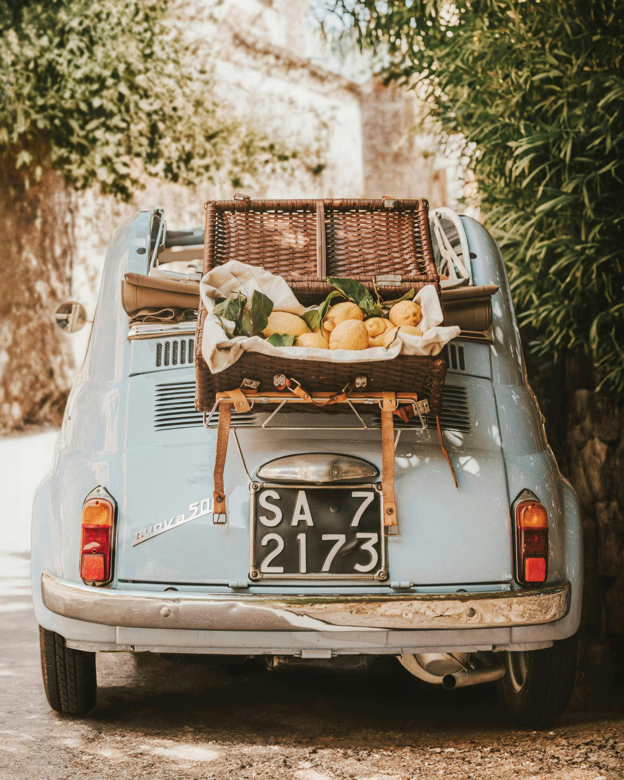 Poster auto vintage blu con cesto da picnic e limoni in strada alberata. Stile retrò italiano.