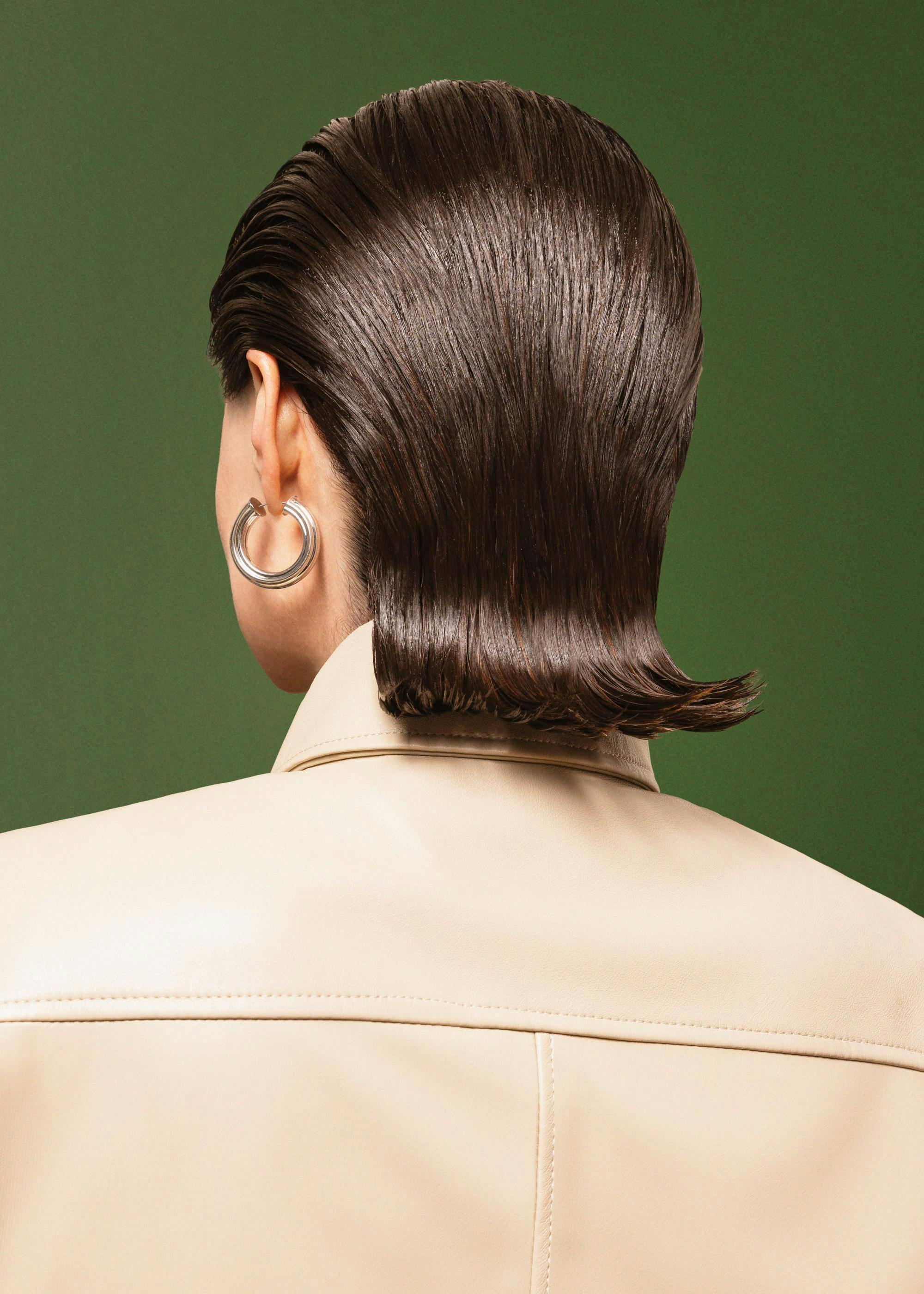 Photography print of a woman with slicked-back hair and hoop earring, seen from behind, against a green background.