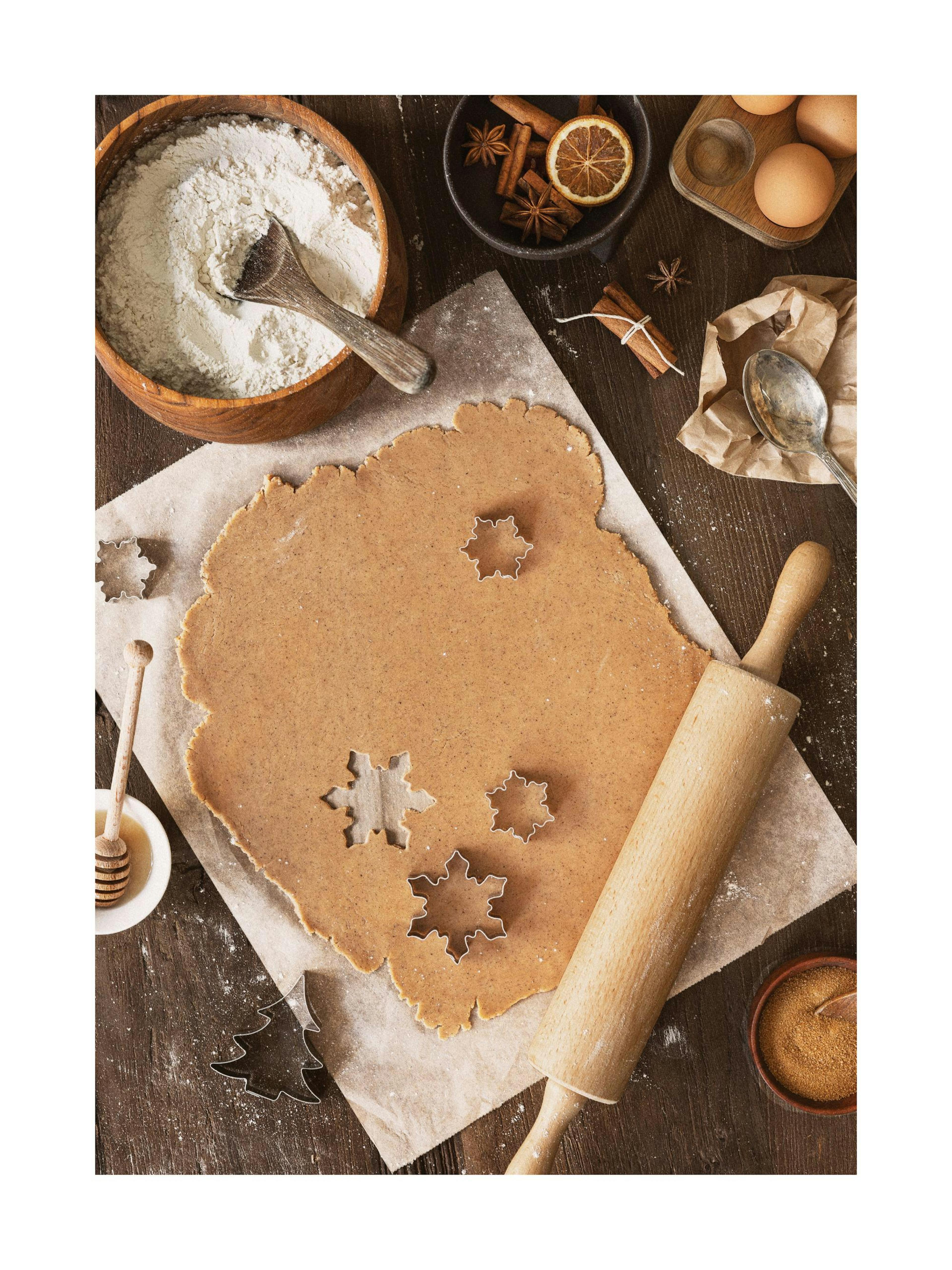 Gingerbread baking scene with dough, cookie cutters, rolling pin, flour, and spices on a wooden table, holiday festive.