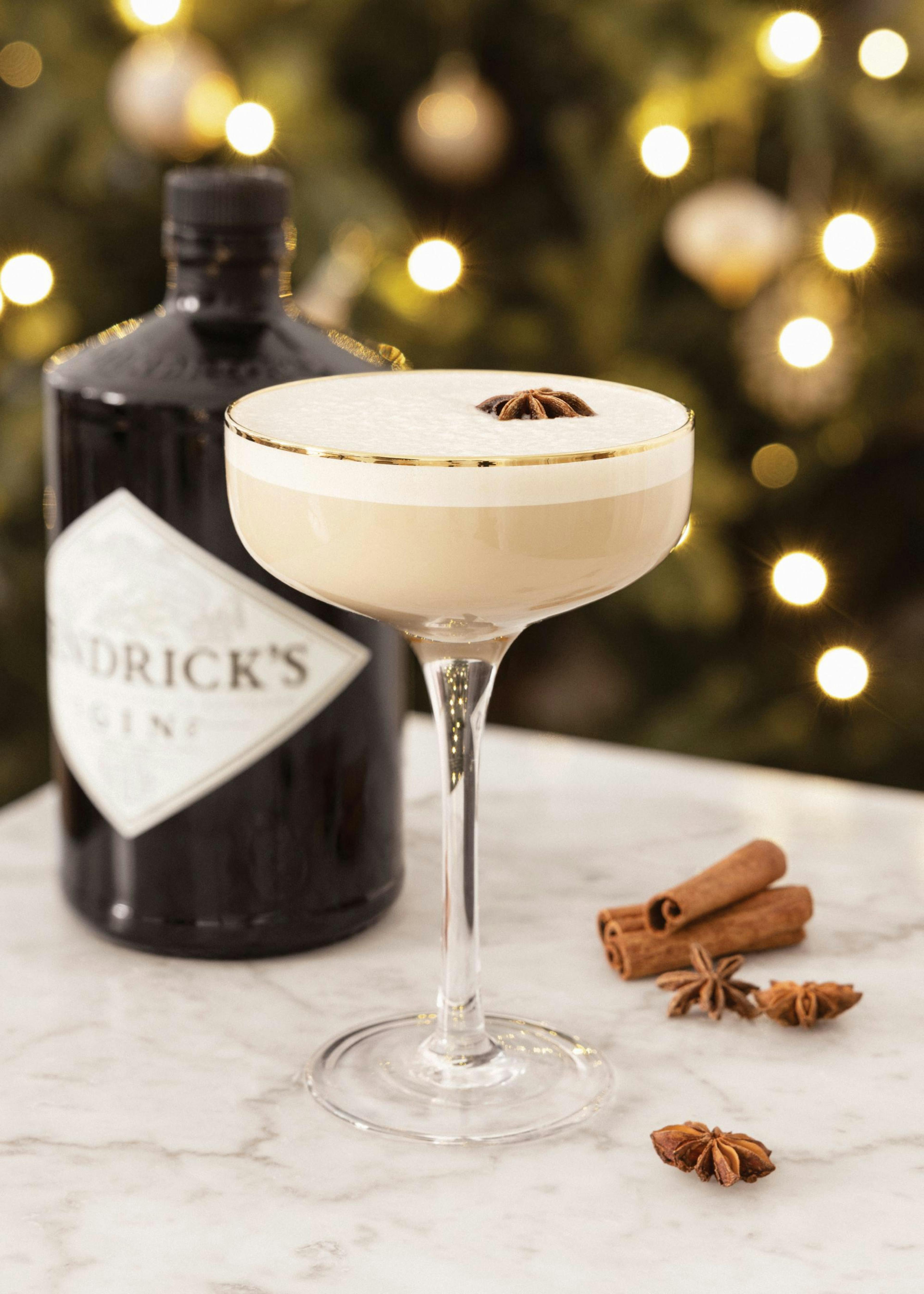 Vánoční plakát s koktejlem eggnog a lahví Hendricks Ginu, ozdobený badyánem a skořicí na mramorovém pozadí.