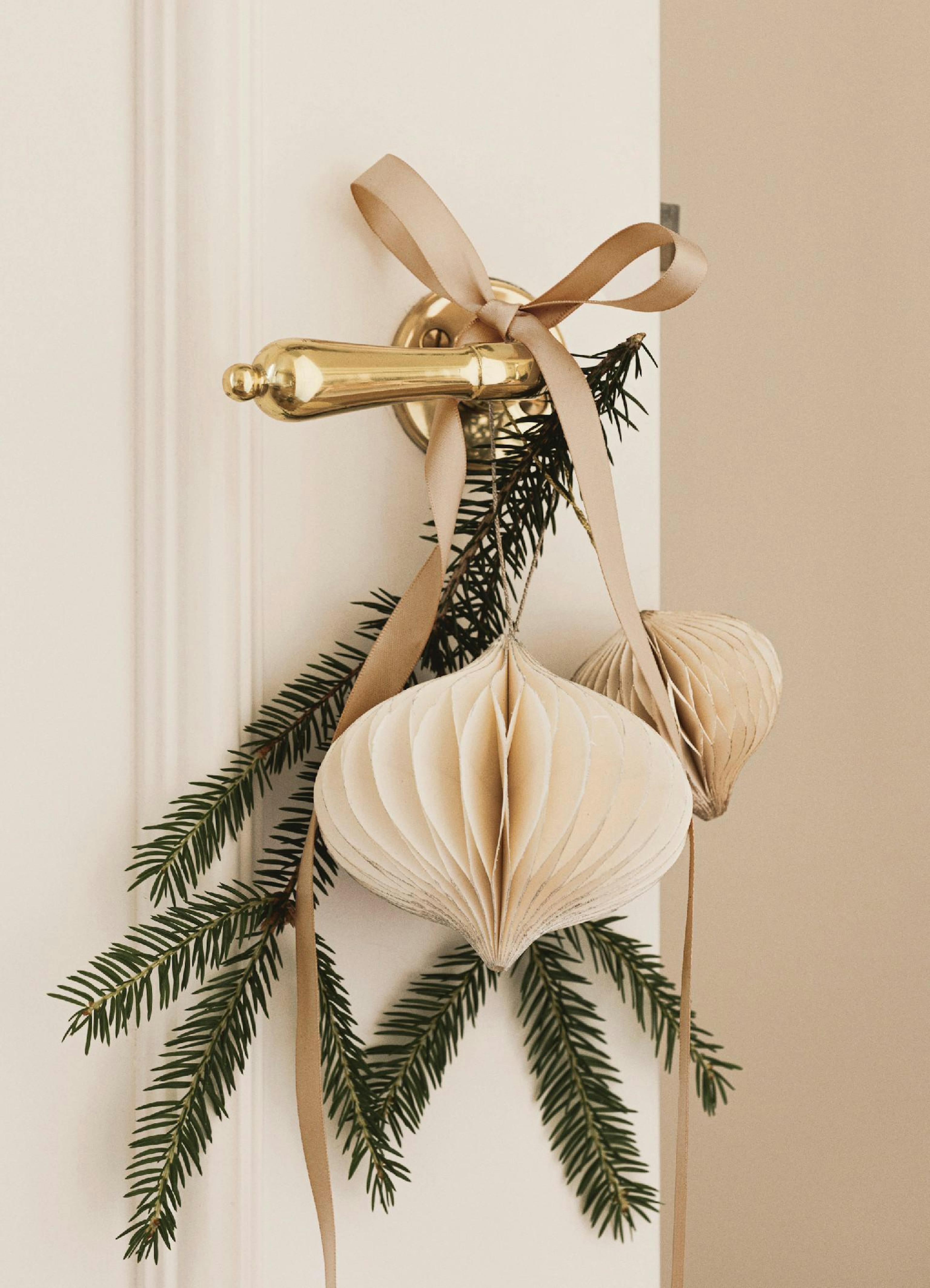 Pomo de puerta dorado con decoraciones de papel beige, cintas marrones y ramas de pino verde, ambiente festivo.