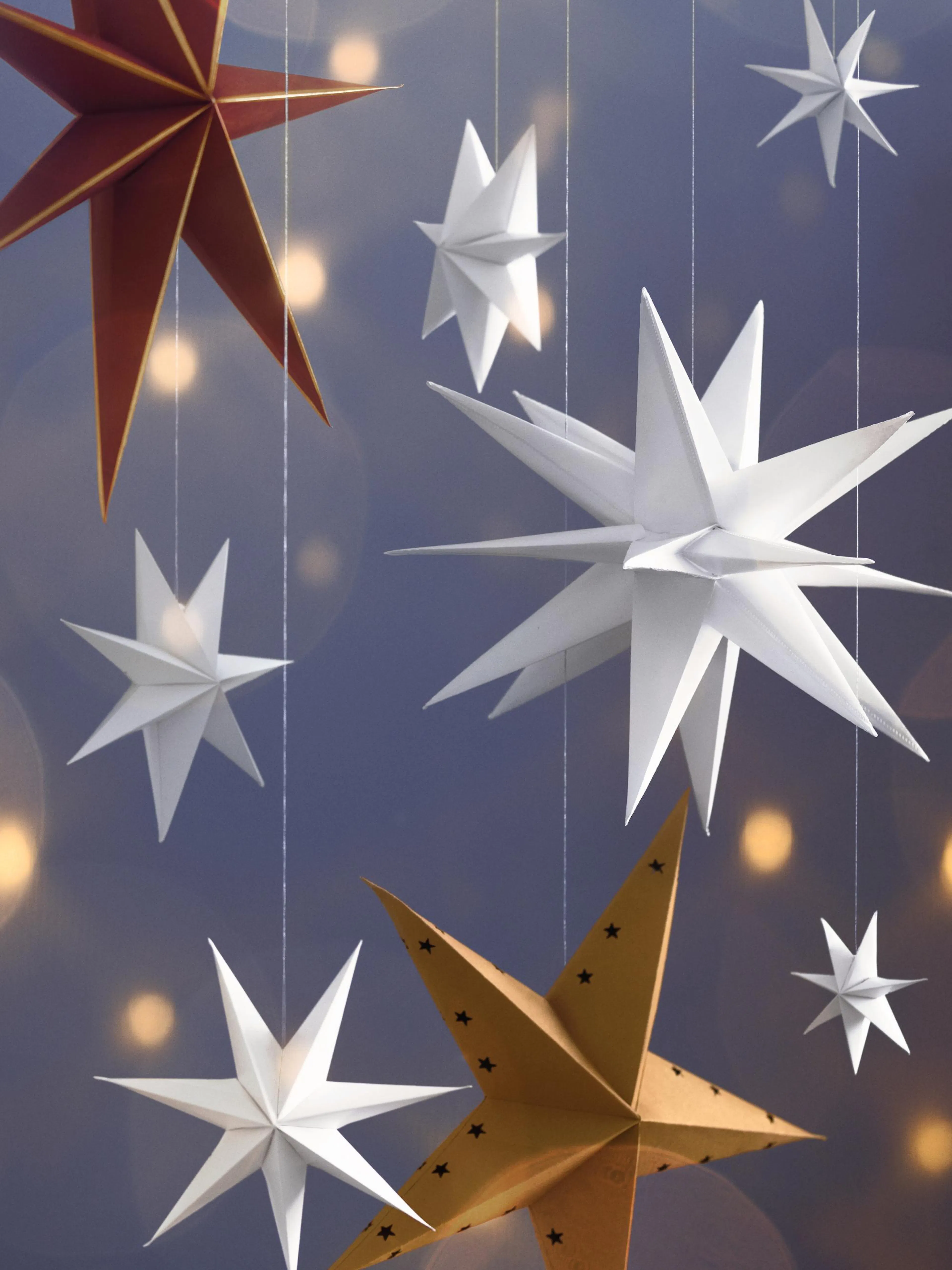 Póster de estrellas de papel colgantes, blancas, rojas y doradas, sobre un fondo azul con luces amarillas