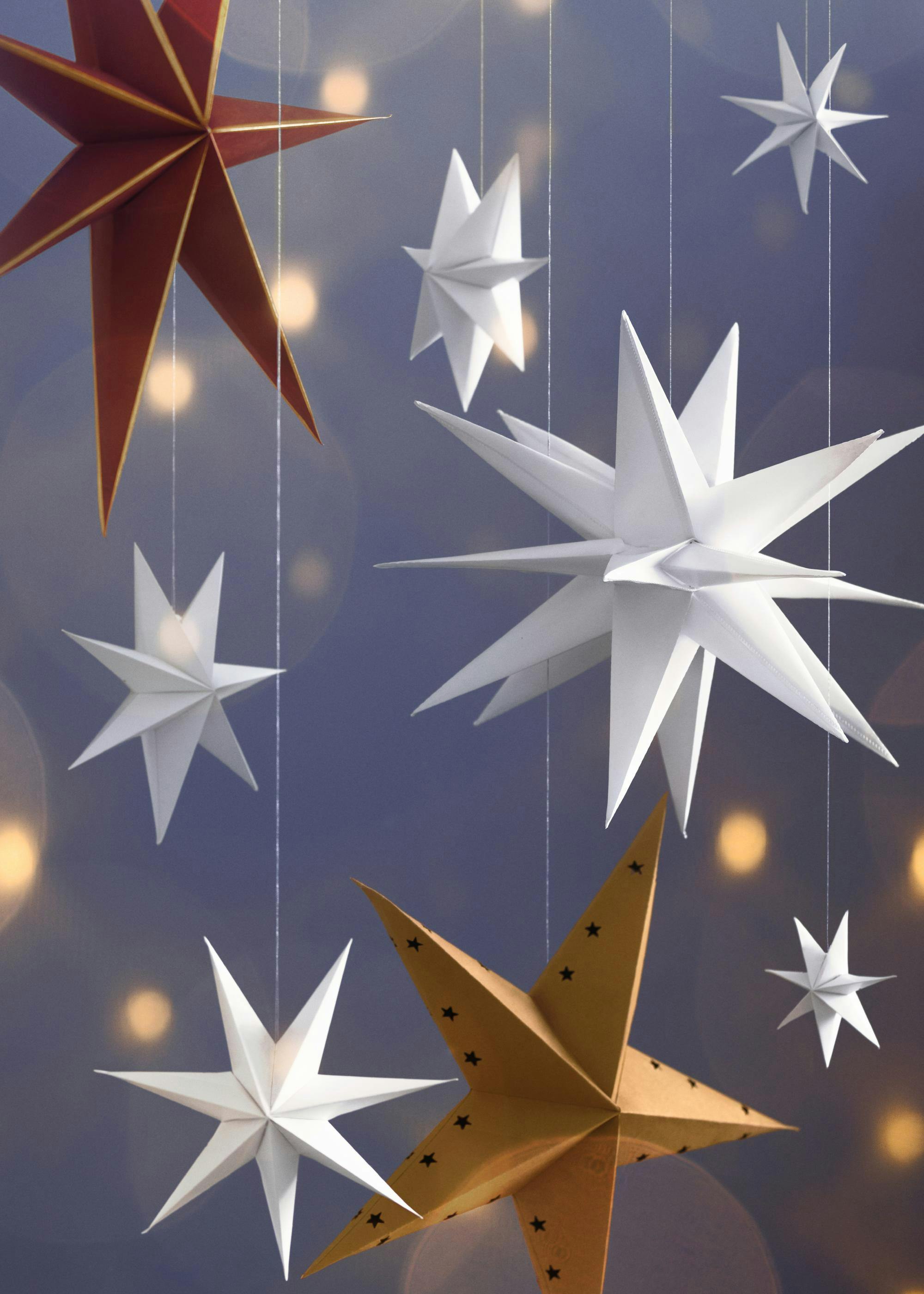 Red, white, and gold paper stars hanging against a blue background with yellow lights in a festive stars print.