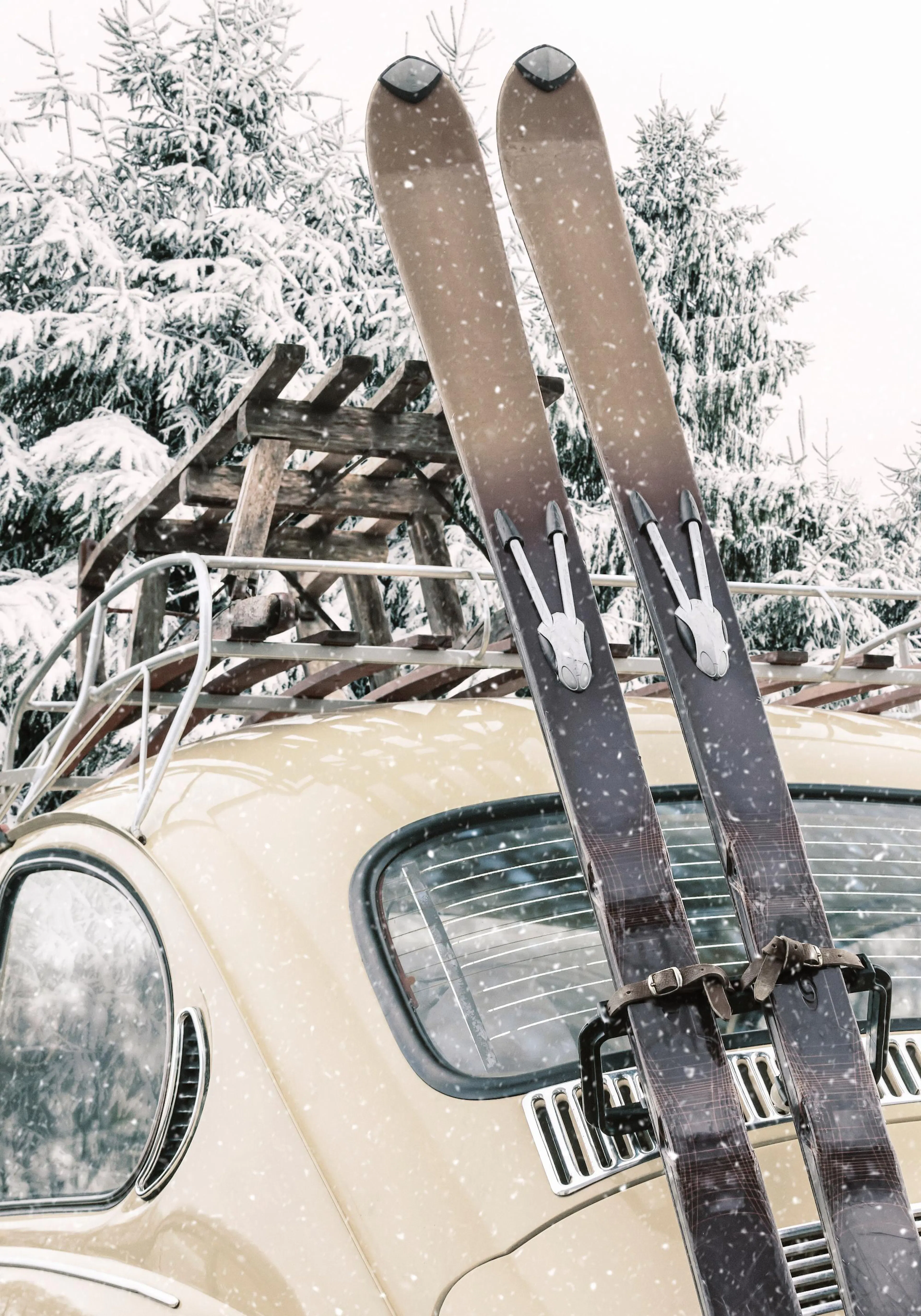 Vintage car with skis on roof, parked in snowy forest with falling snow, evoking winter charm