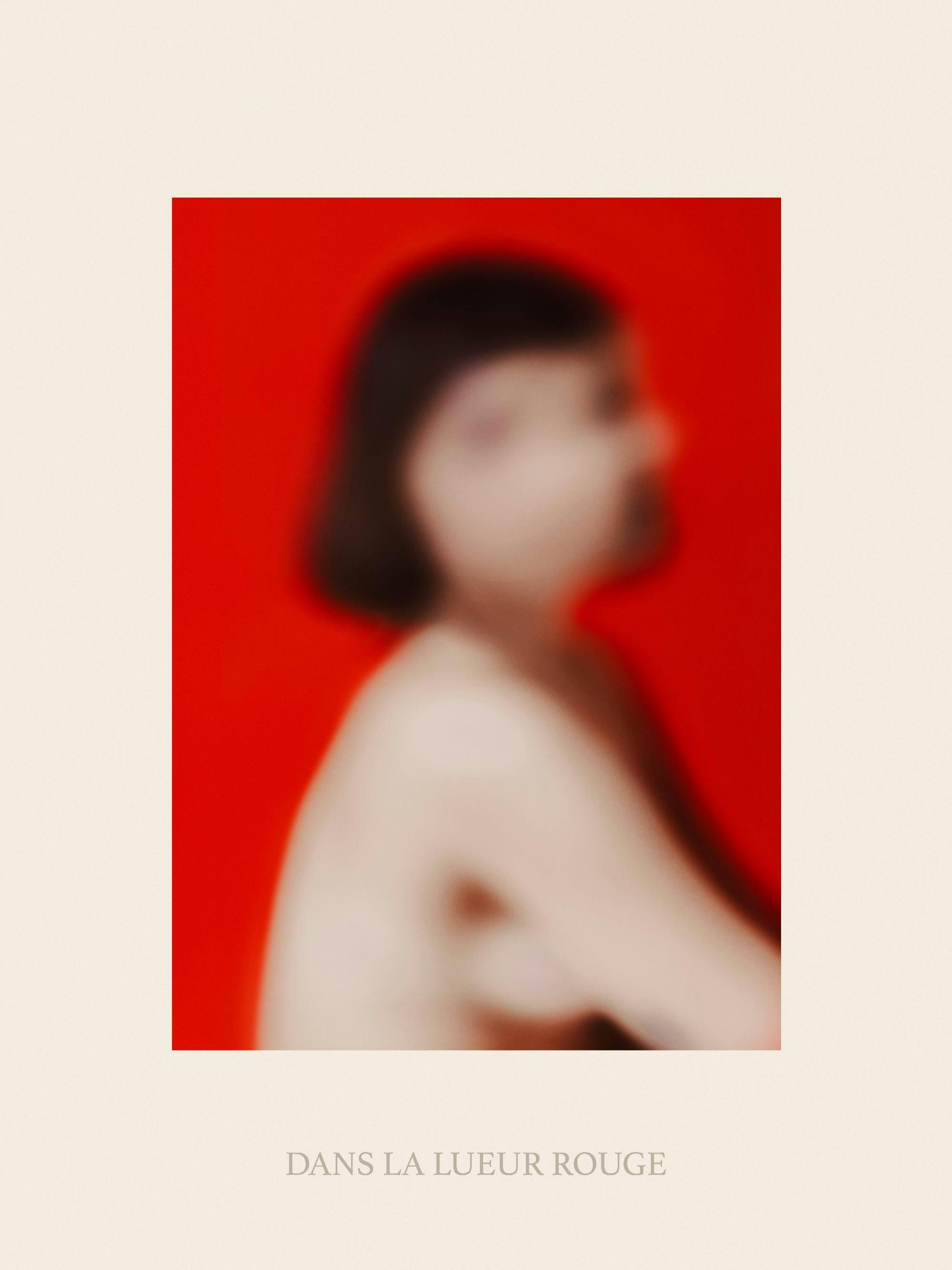 Poster: Unscharfes Porträt einer Frau mit dunklen Haaren vor rotem Hintergrund, daneben in Grau DANS LA LUEUR ROUGE.
