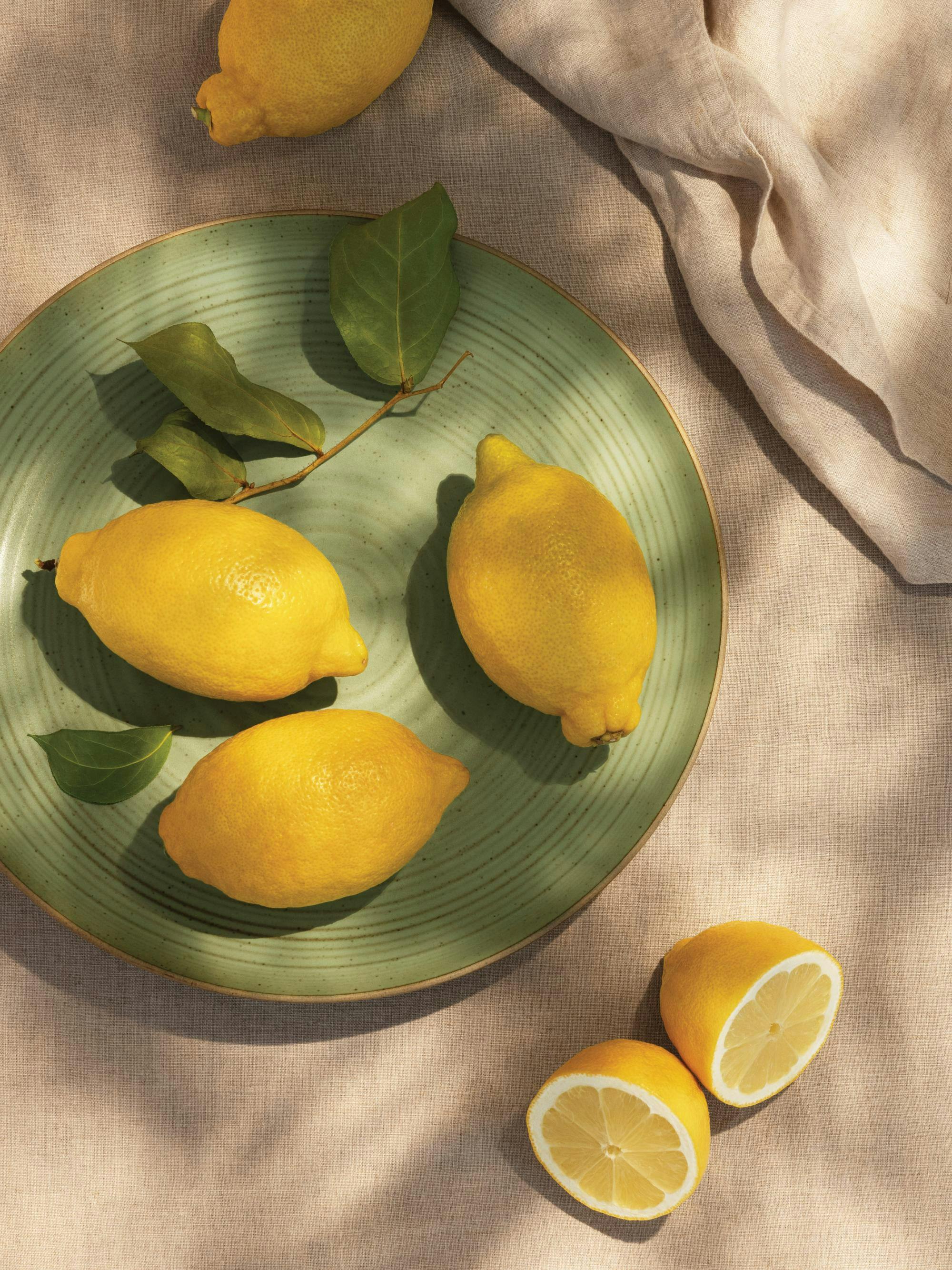 Een poster met citroenen op een groene schaal met bladeren op een lichte beige ondergrond.