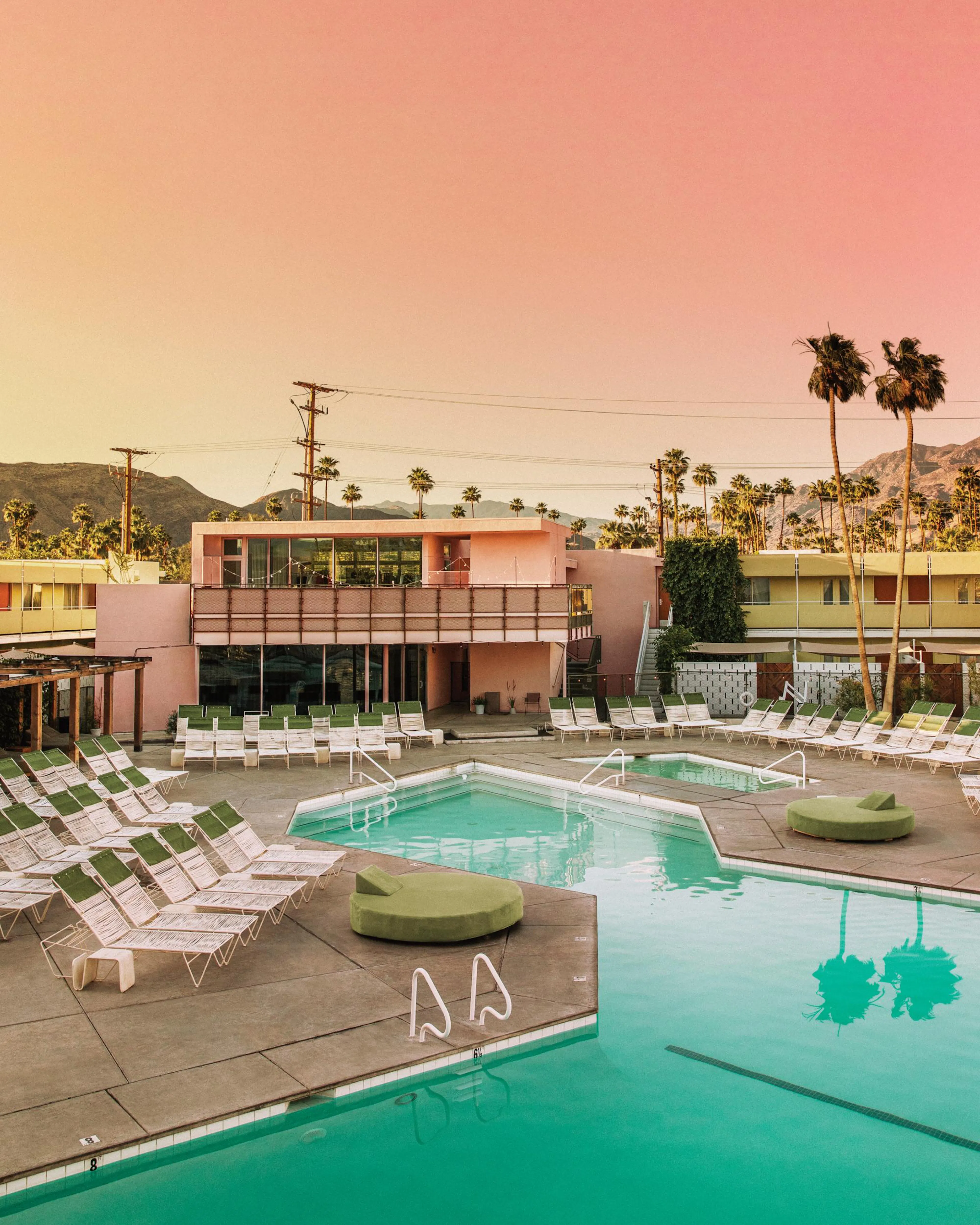 A mid-century modern pool print with pink buildings, palm trees, and aqua water, reflecting the sunset.