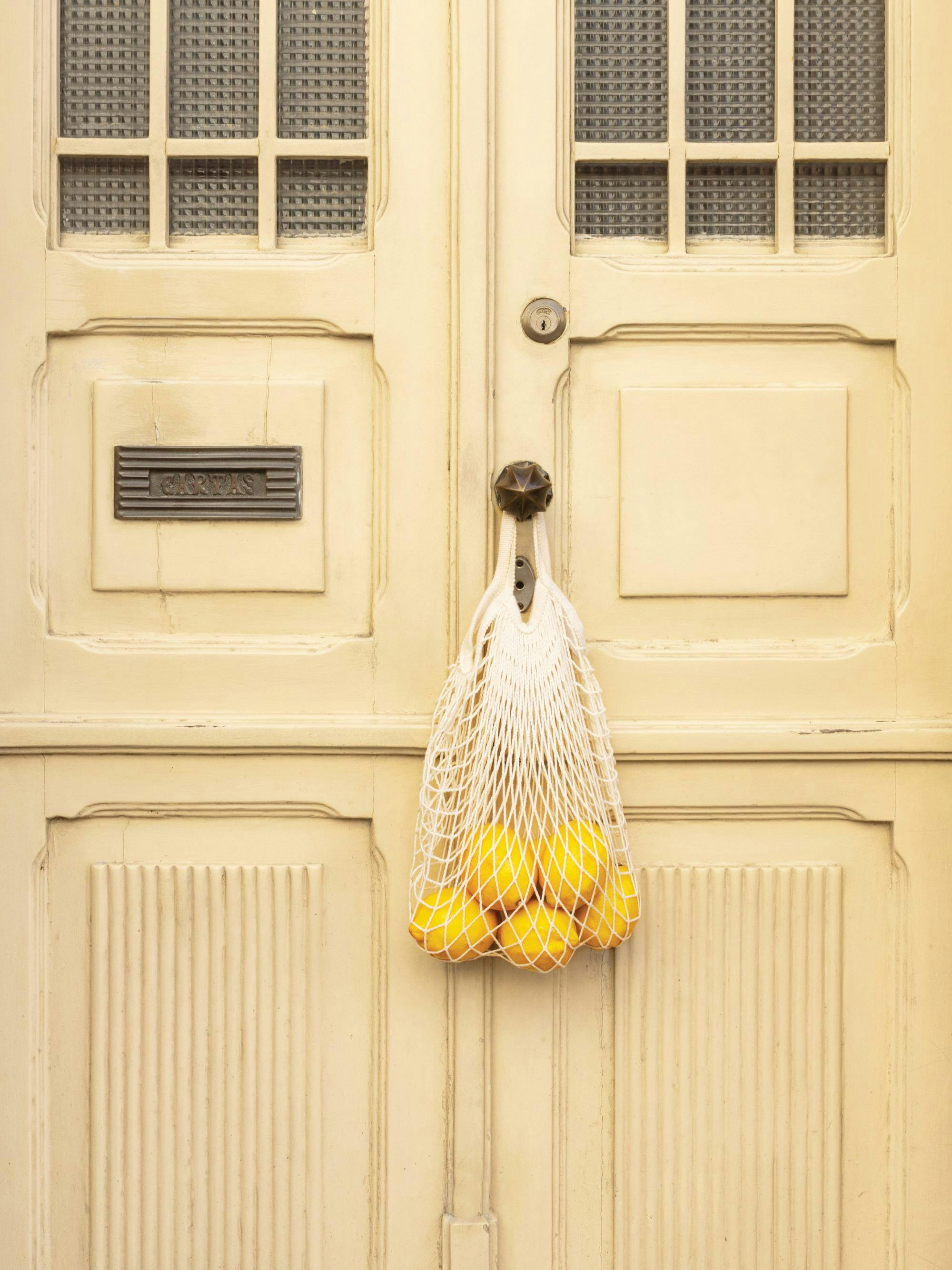 En poster av en ljusgul dörr med en nätkasse fylld med gula citroner hängandes på handtaget.
