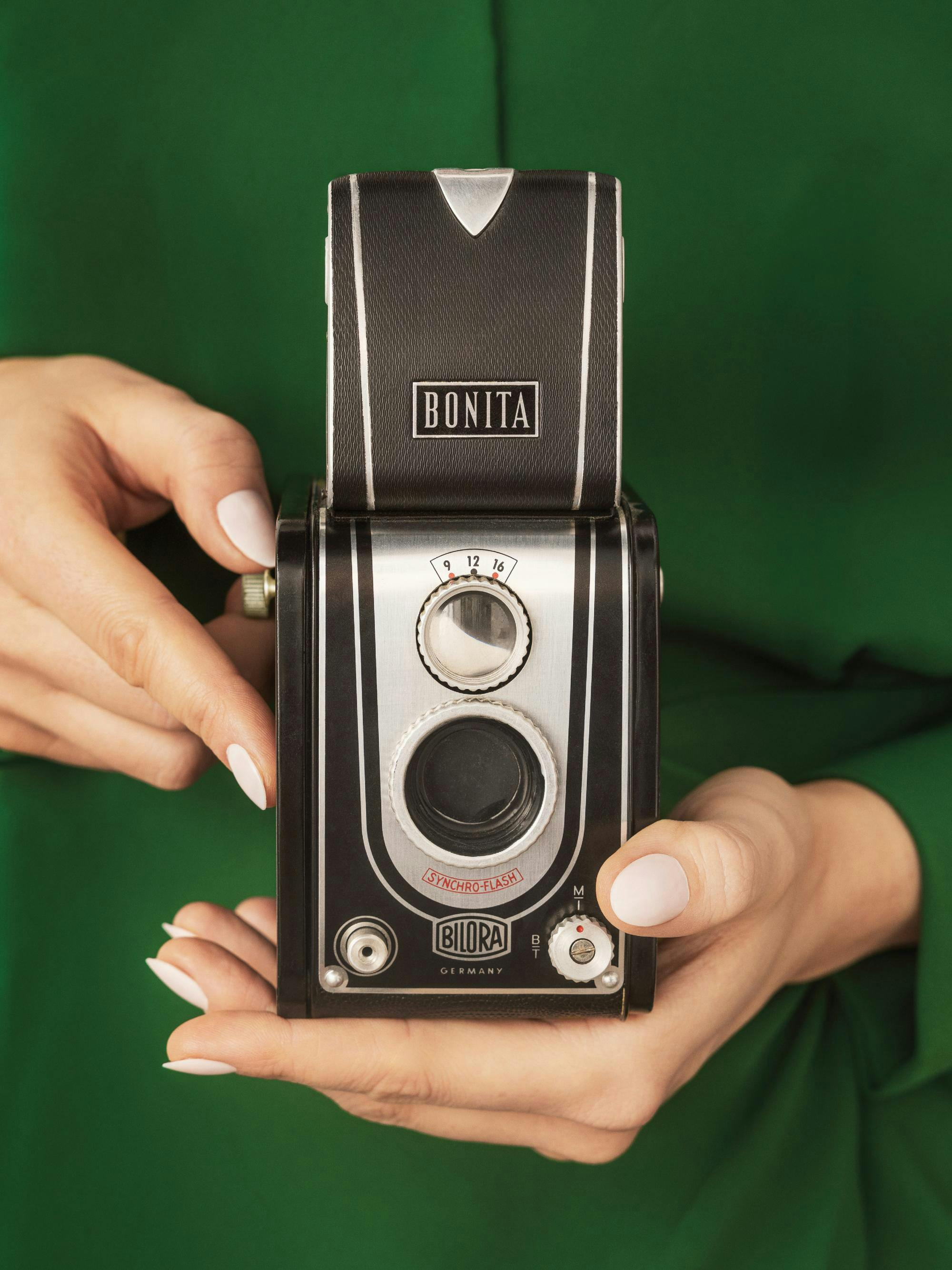En poster av en person som håller en klassisk svart och silverfärgad vintagekamera mot en grön bakgrund.