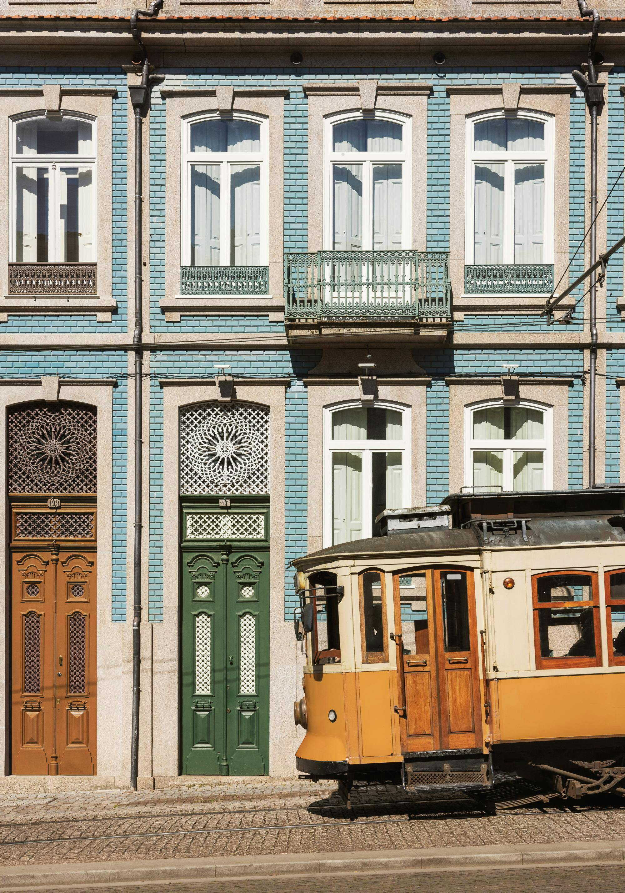 En poster av en gul spårvagn på kullersten med en ljusblå byggnad i bakgrunden.