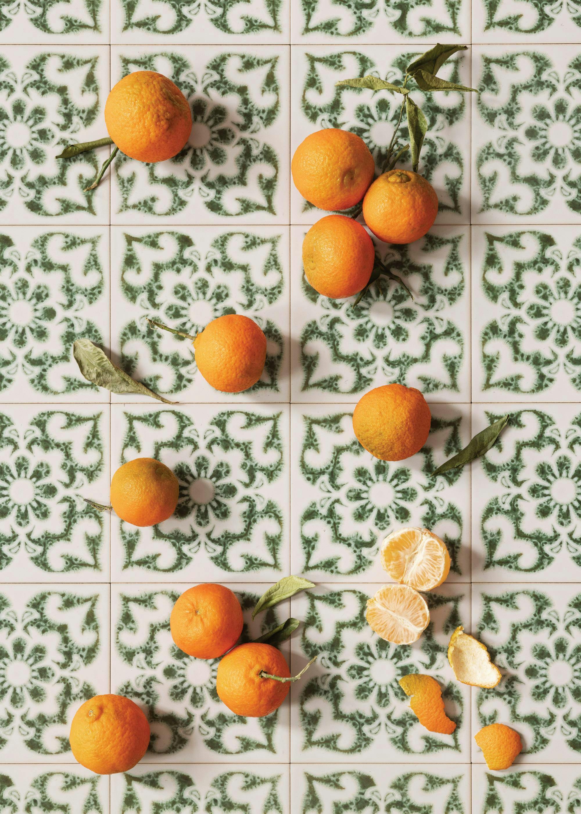 A top-down print of multiple tangerines, some with leaves, on white tiles with a green floral pattern.