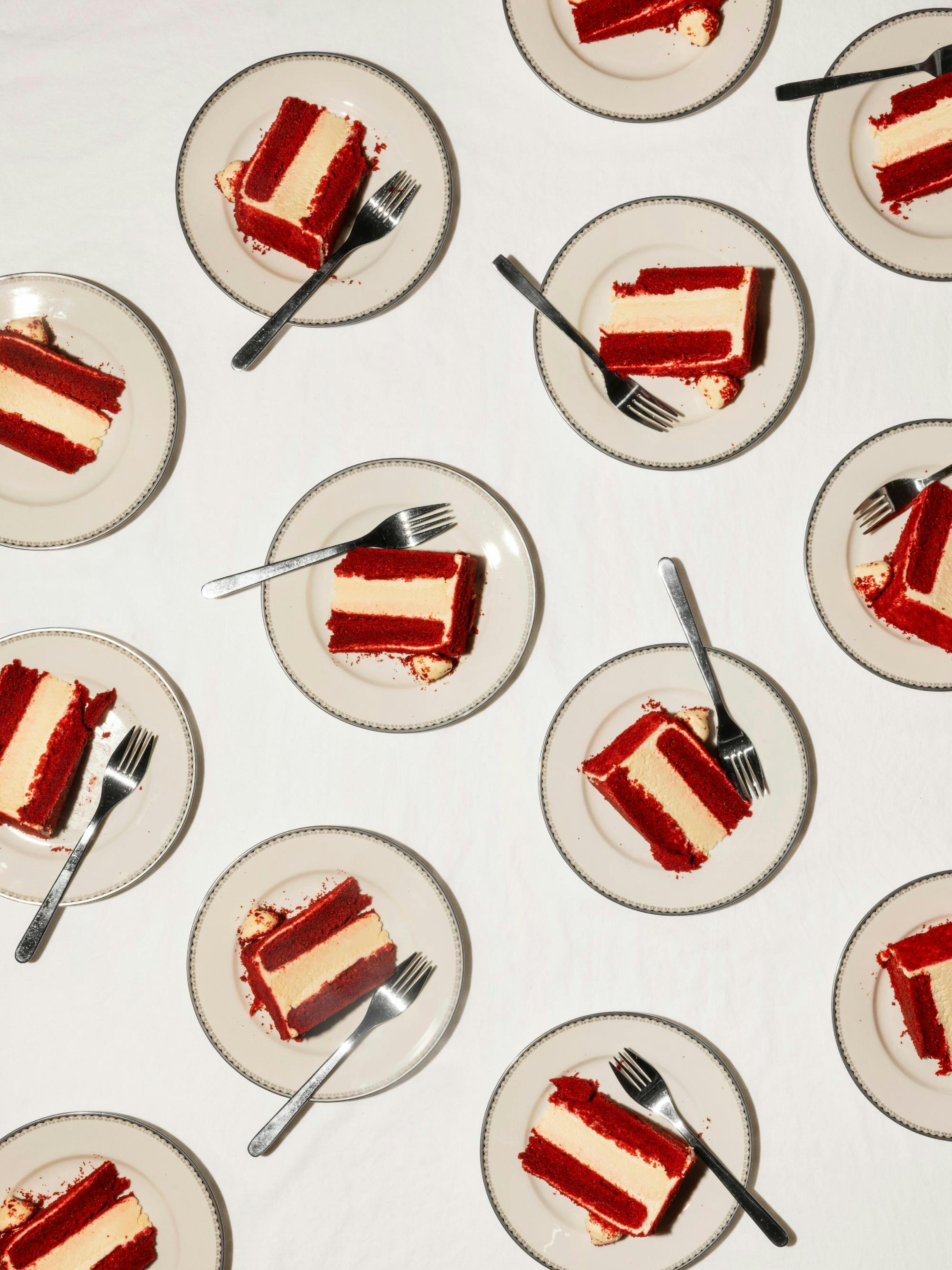 Plagát s koláčmi red velvet na tanieroch s vidličkami, visí v jedálni nad dreveným stolom s kávovarom a vázou.