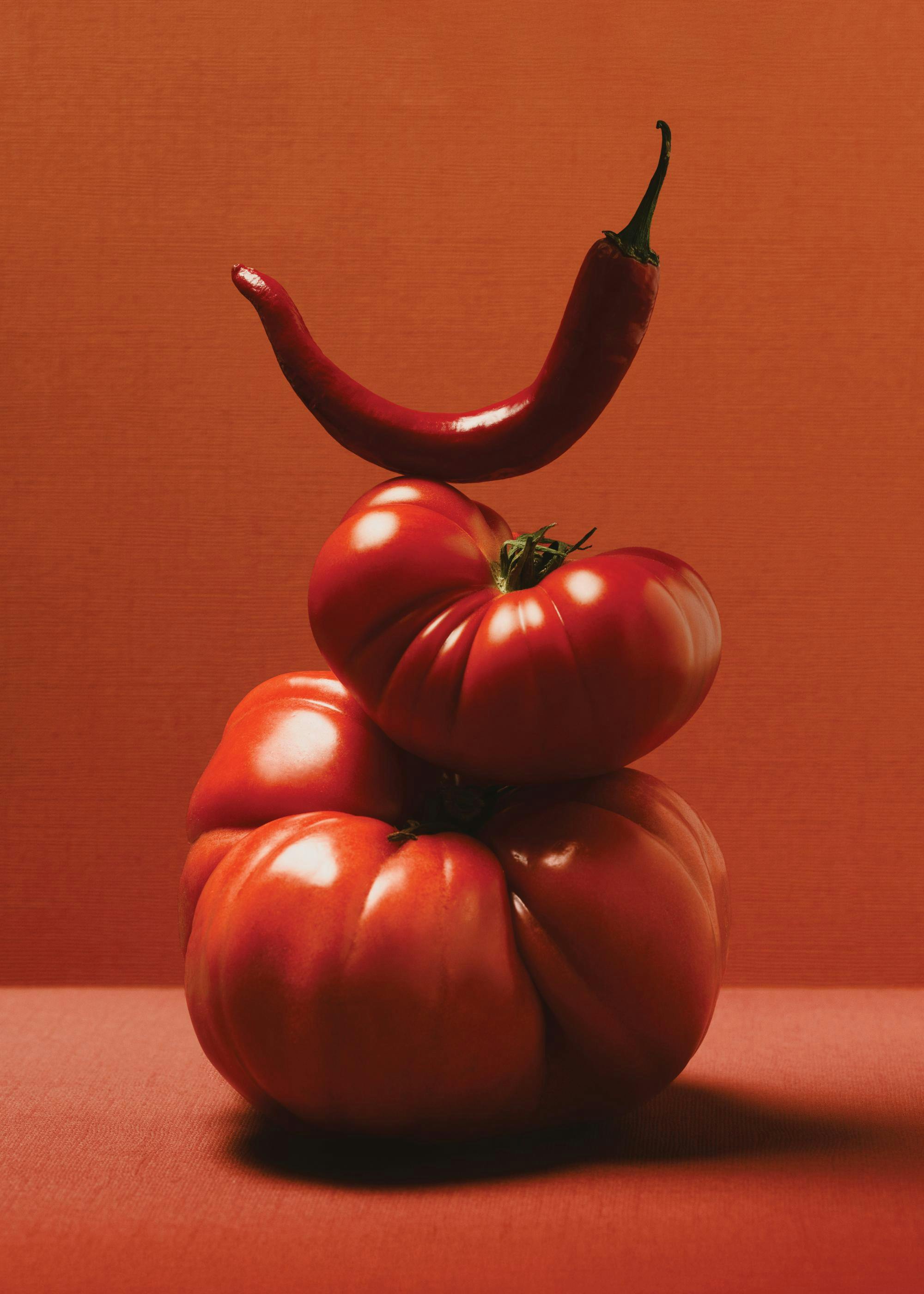 Poster mit roter Paprika auf gestapelten roten Ochsenherz-Tomaten vor einem monochromen Hintergrund.
