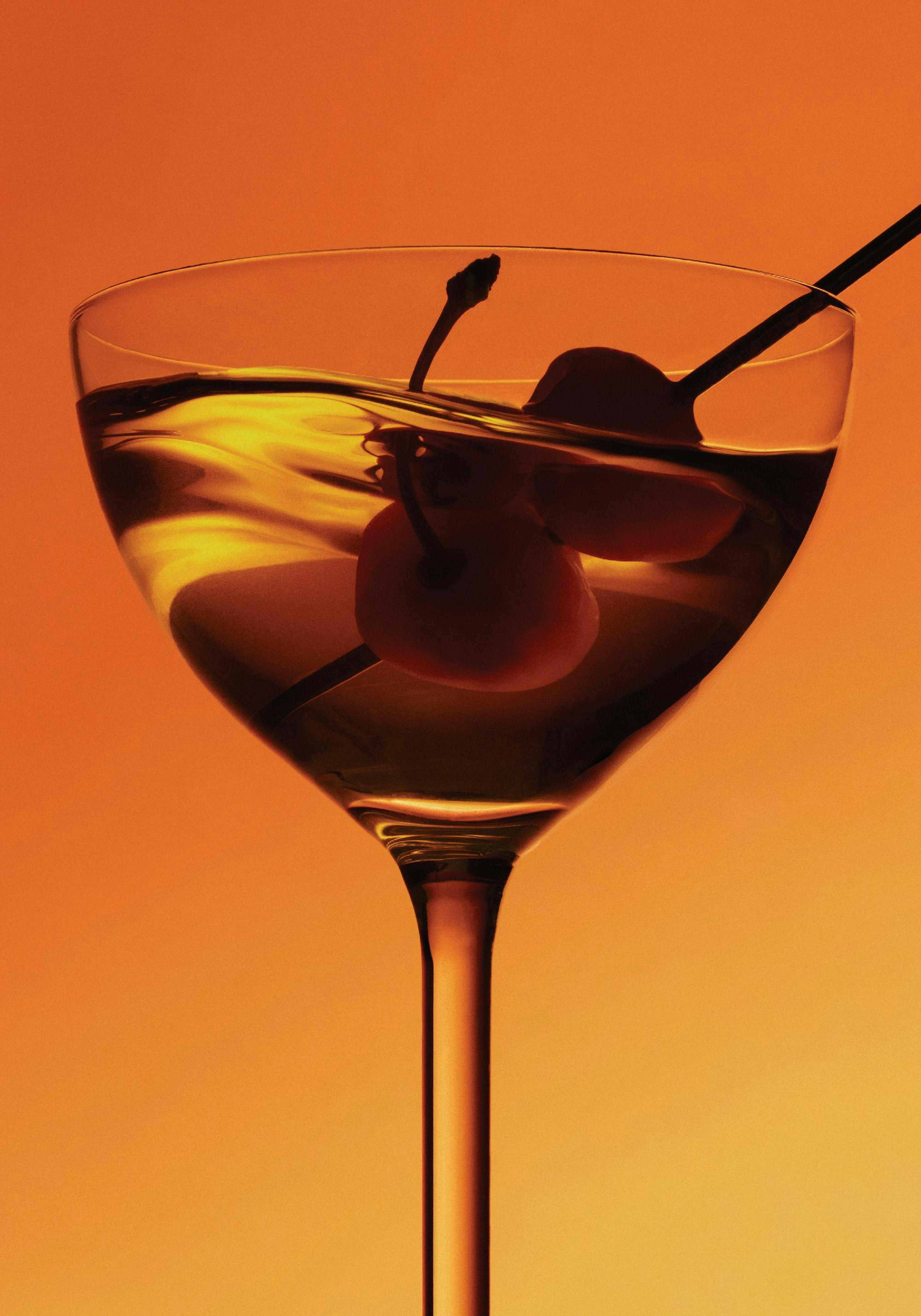 A low-angle print of a martini glass with two cherries and a stirrer, set against a warm orange background.