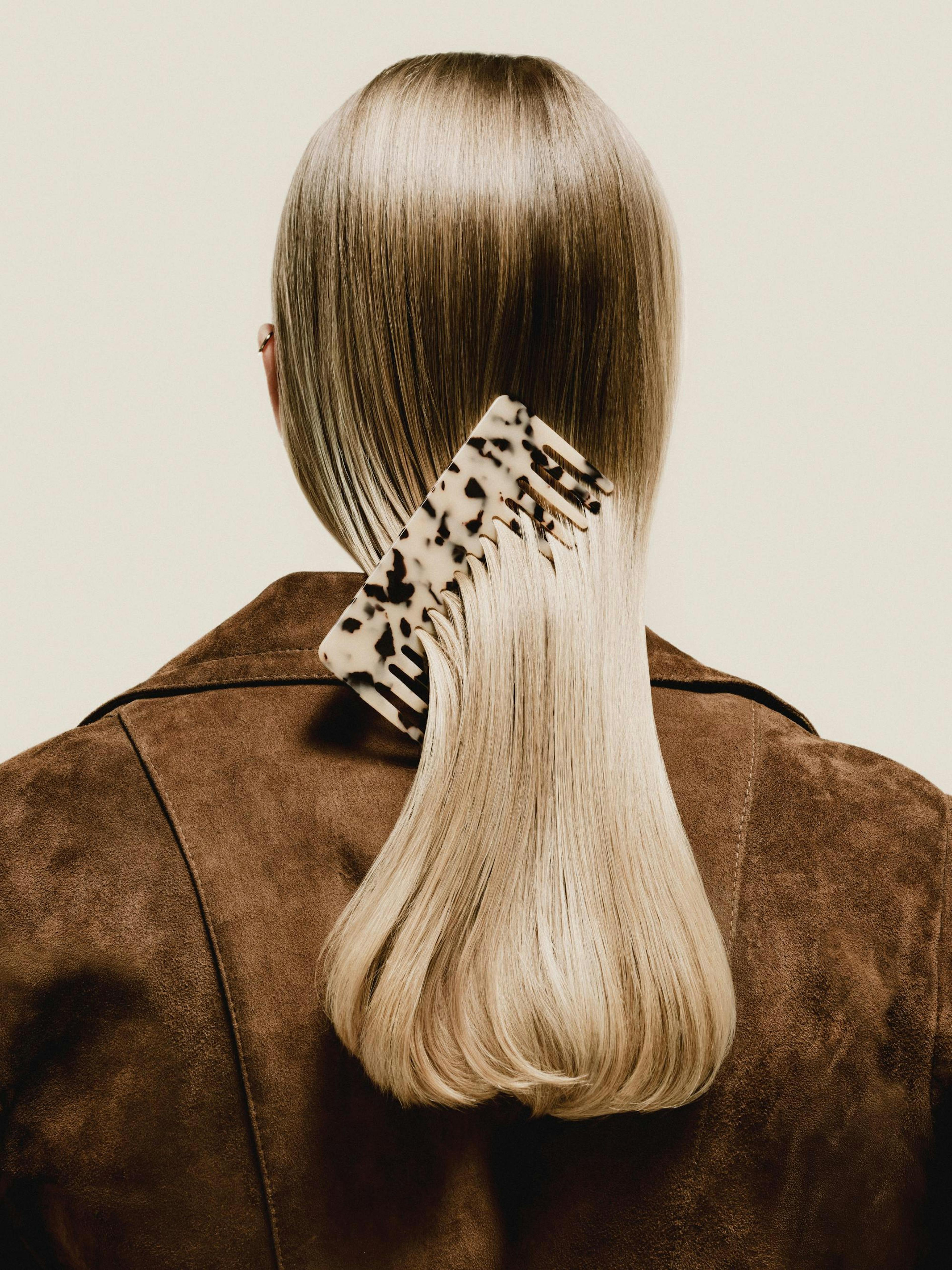 Un póster de la espalda de una mujer con cabello rubio liso y un peine de concha de tortuga en el cabello, vestida con una chaqu