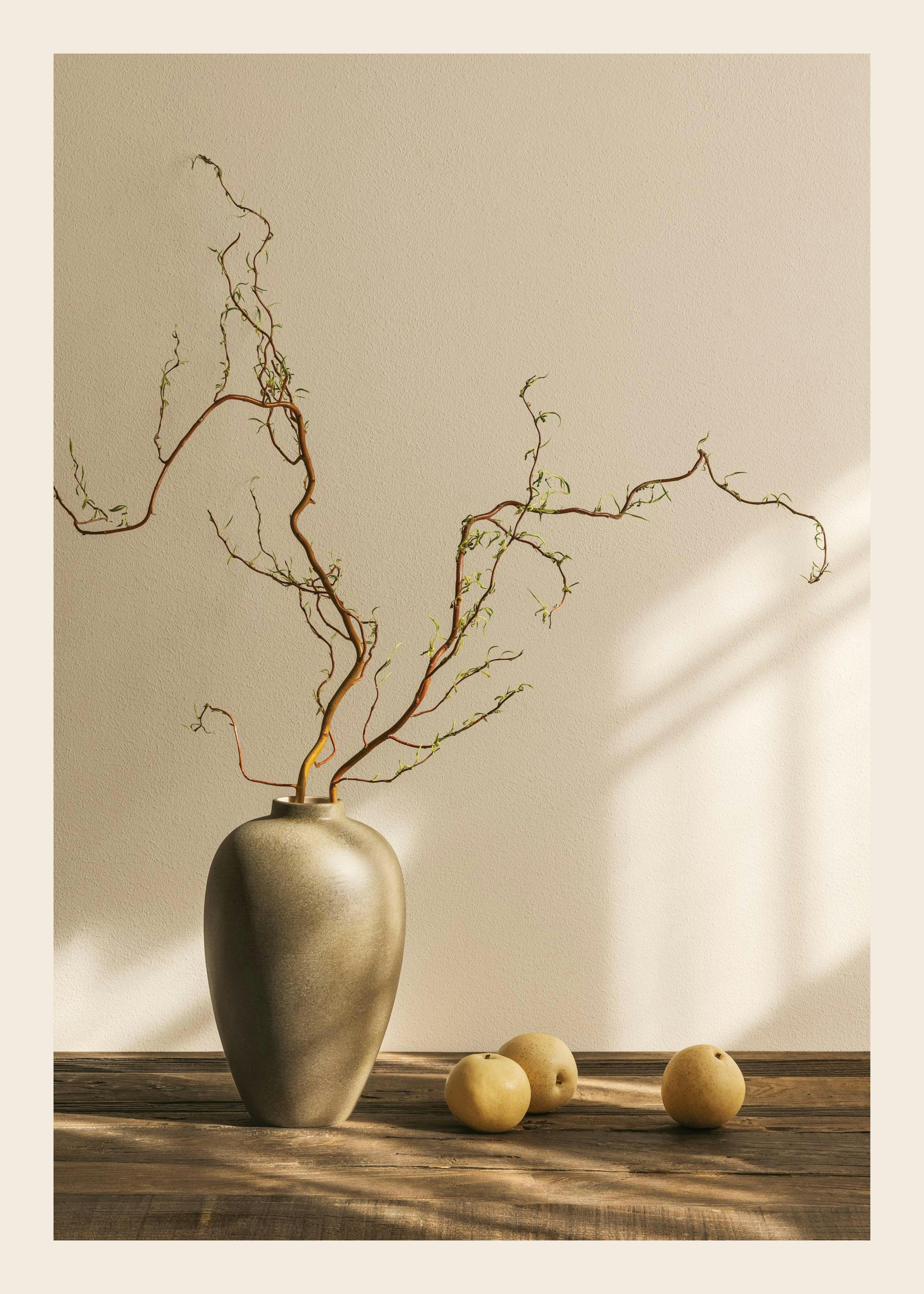 Poster de vaso cinzento com ramos finos e três peras asiáticas sobre uma mesa de madeira rústica.