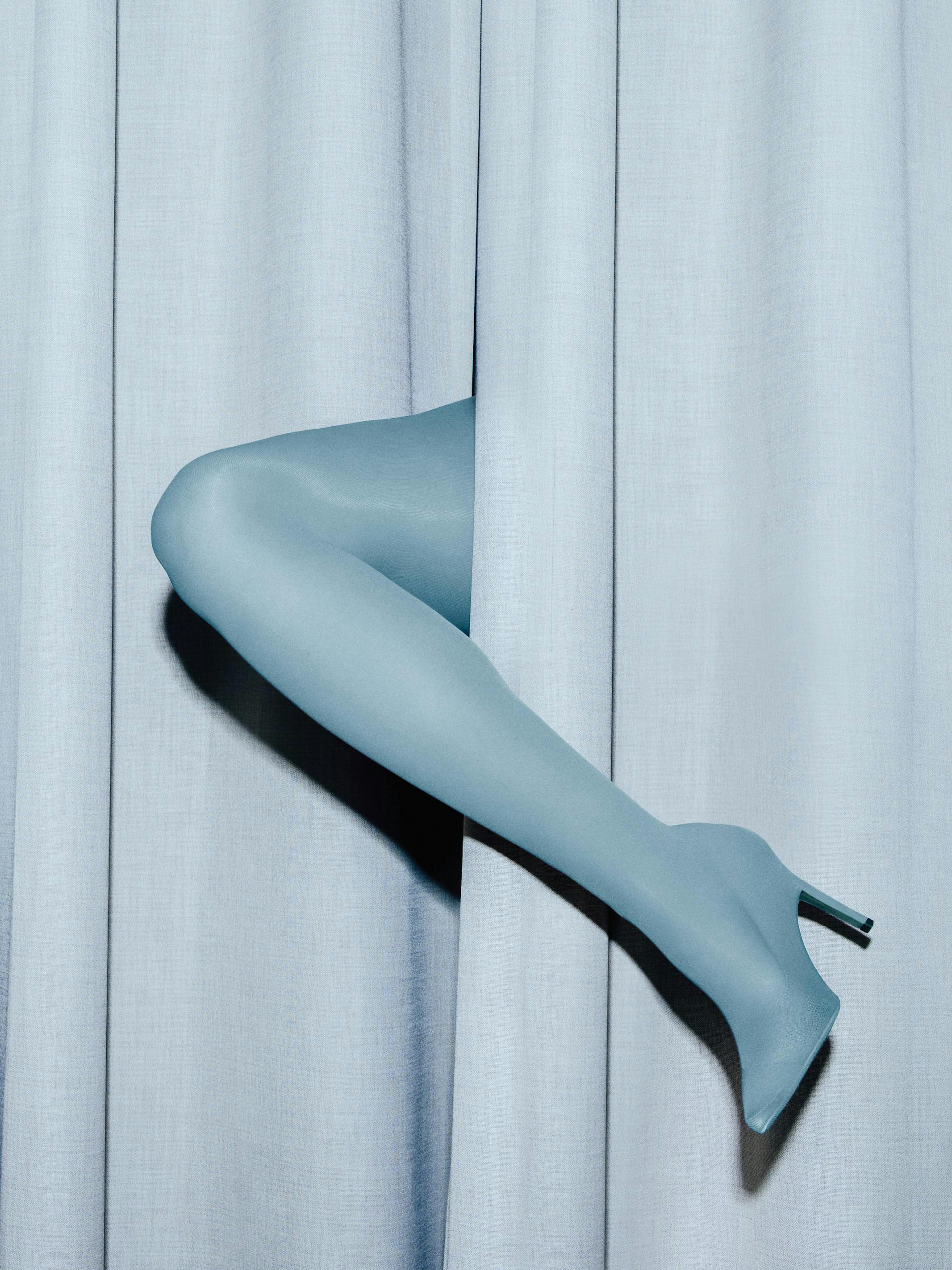 Póster de una pierna femenina azul claro con tacón asomándose por una cortina del mismo color.