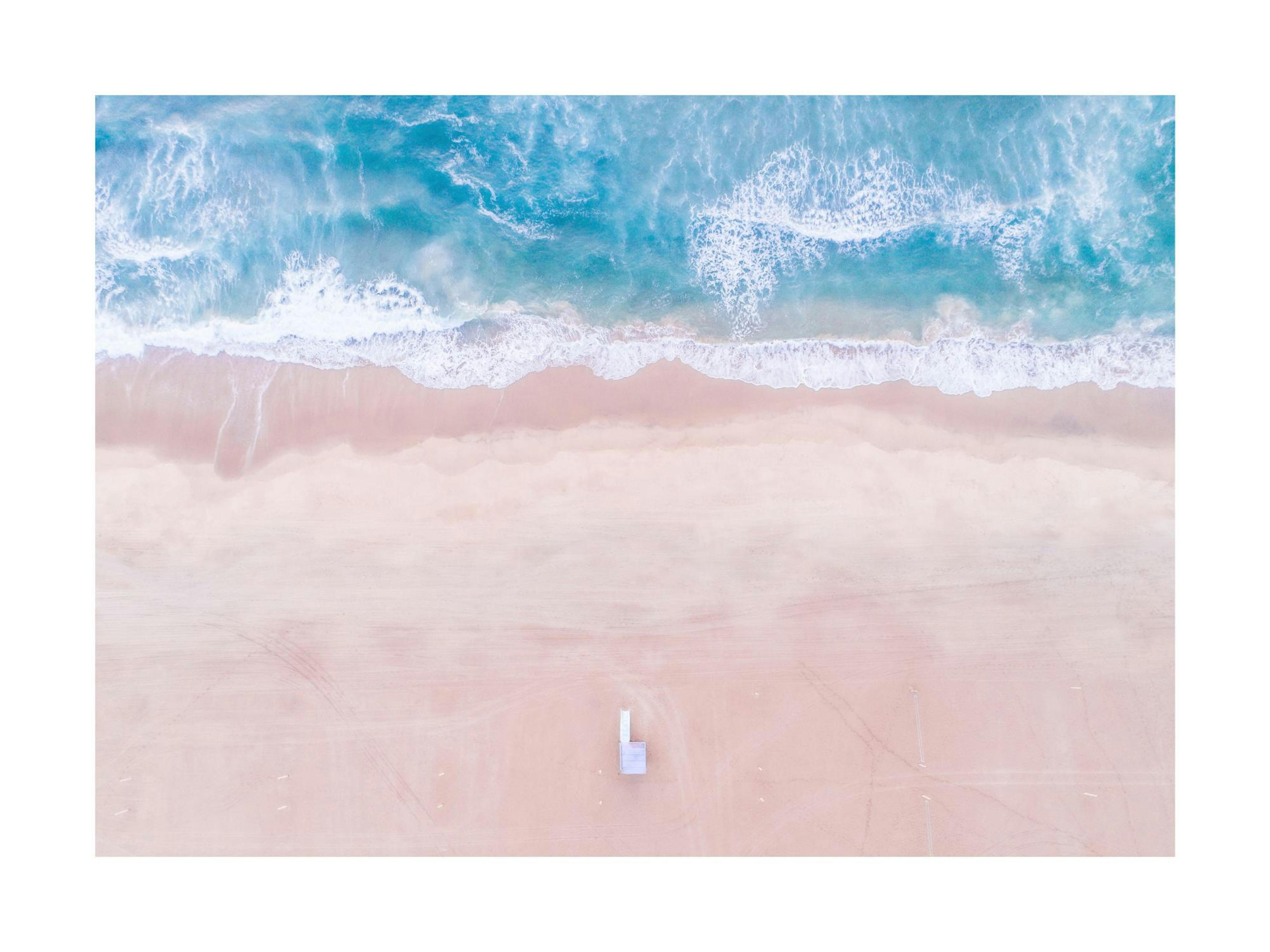 Flygfoto över rosa strand med turkost hav och vita vågor.