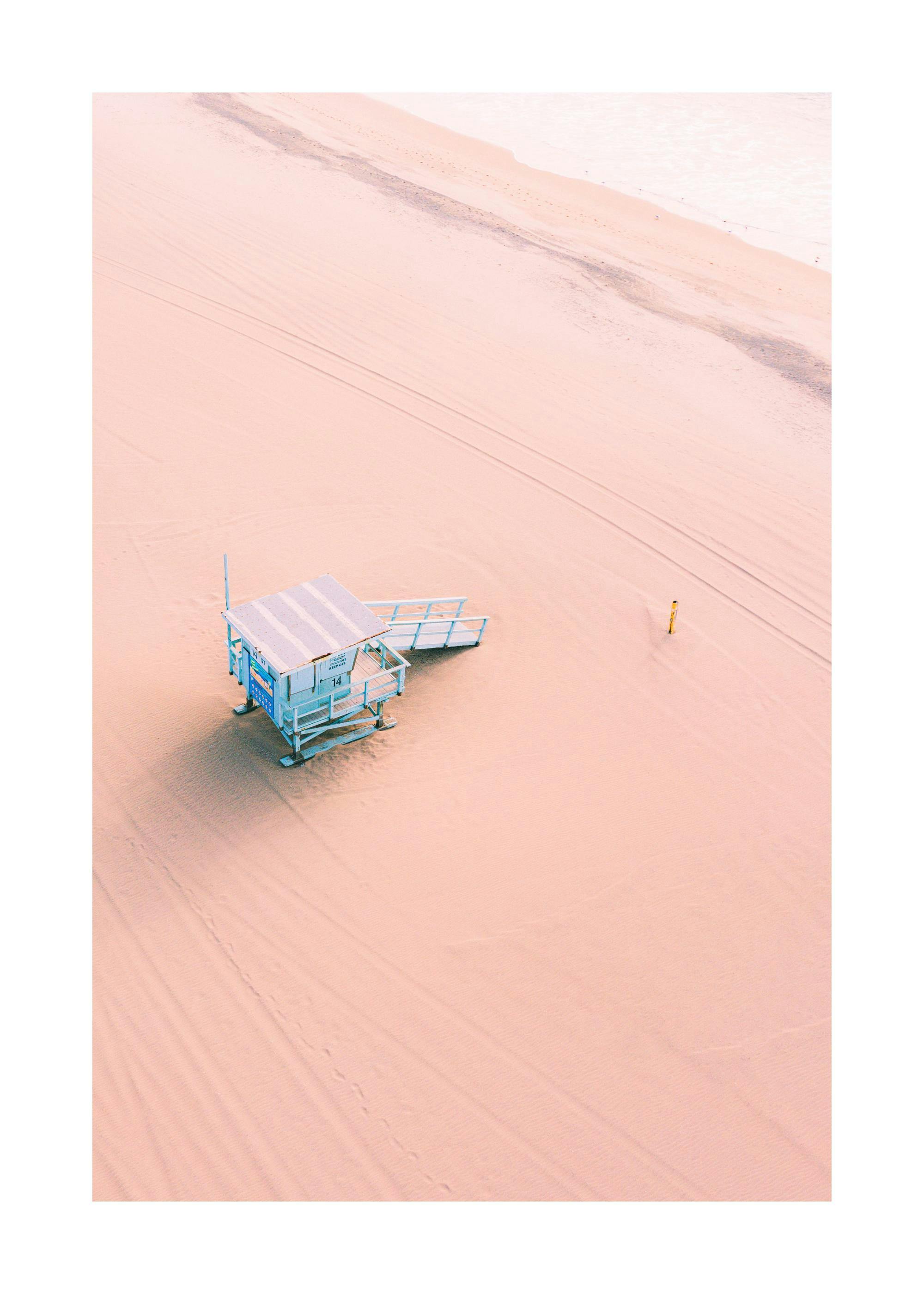 Richard Podgurski Poster: Strandfotografie eines hellblauen Strandhauses auf rosafarbenem Sandstrand, minimalistischer Stil.