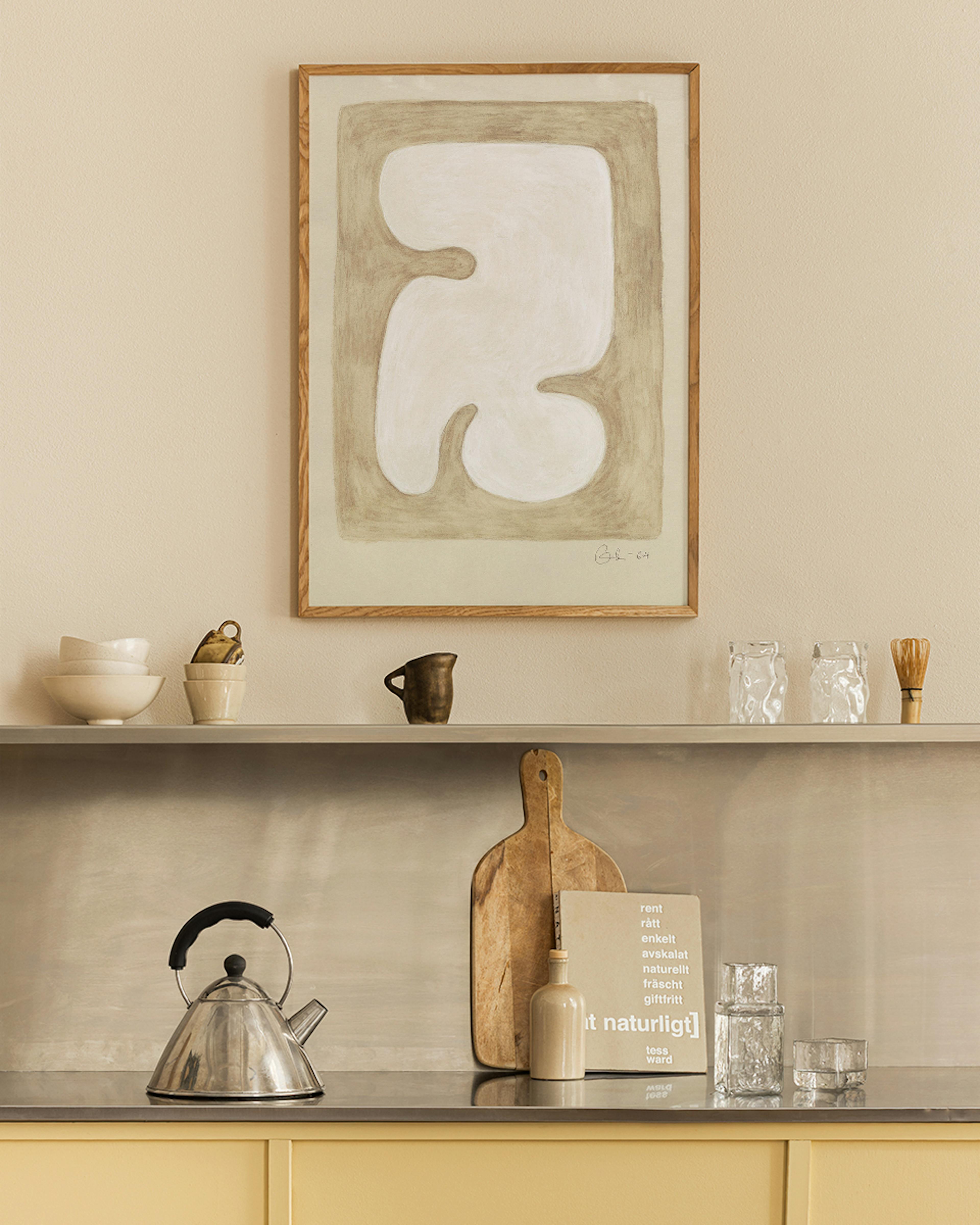 A print of a white organic abstract shape with a beige border, hanging in a minimalist kitchen above shelving.