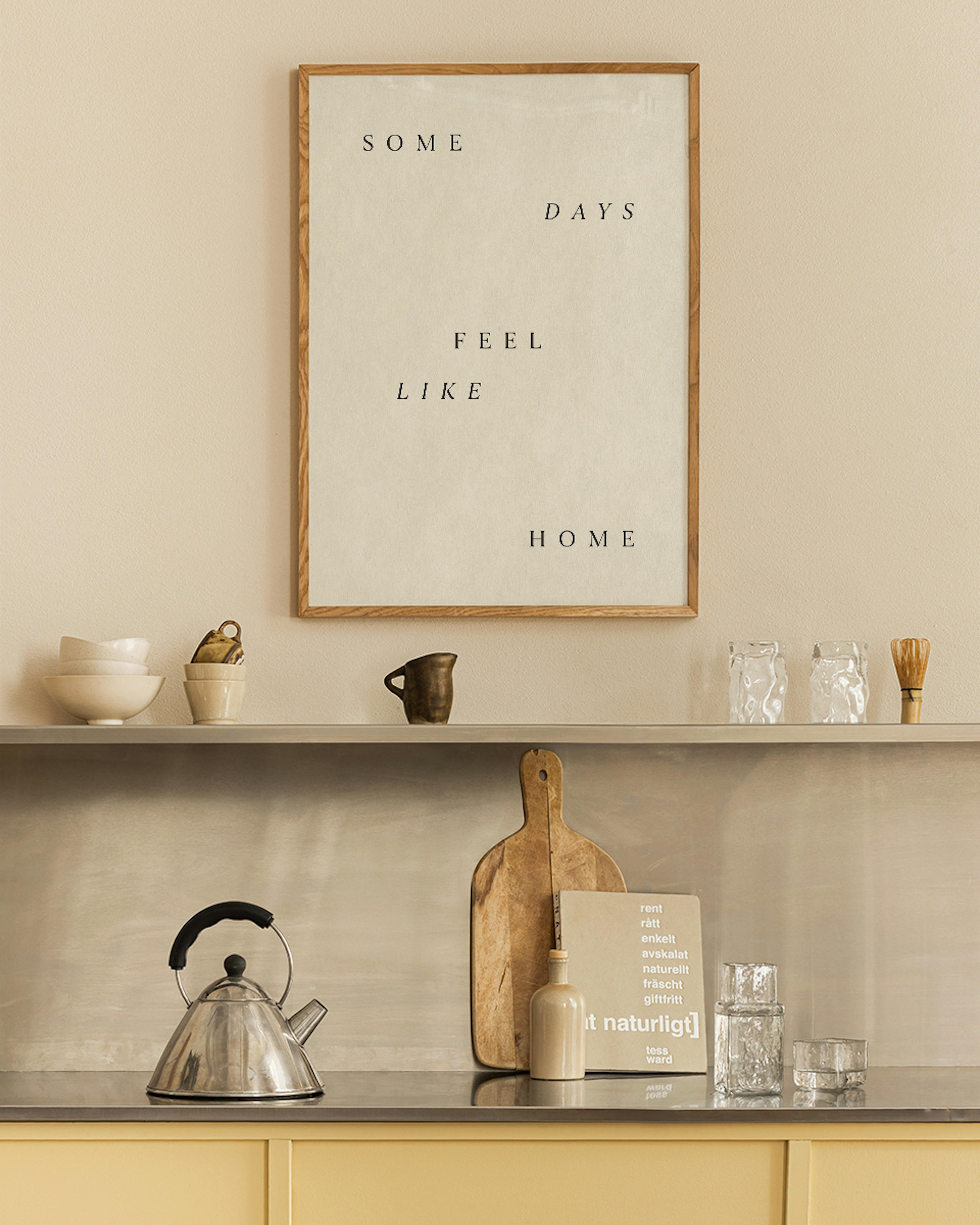 Póster de texto con SOME DAYS FEEL LIKE HOME en un marco de madera, colgado sobre un estante en una cocina.