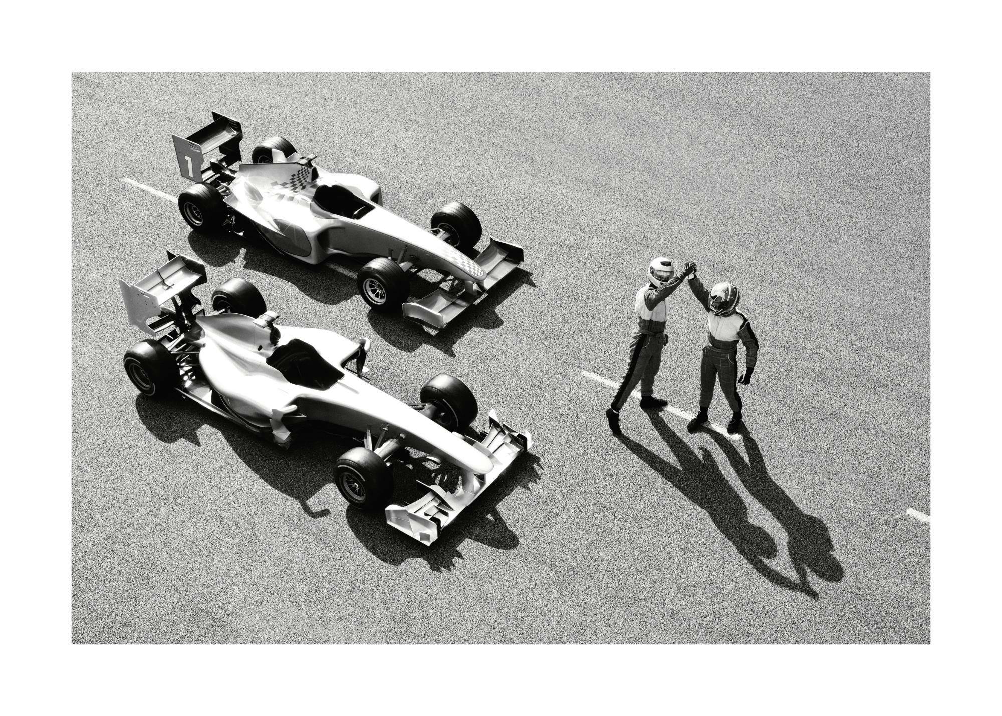 Mustavalkoinen valokuva Formula 1 -kilpa-autoista ja kuljettajista juhlimassa radalla. Urheilullinen valokuvataide.