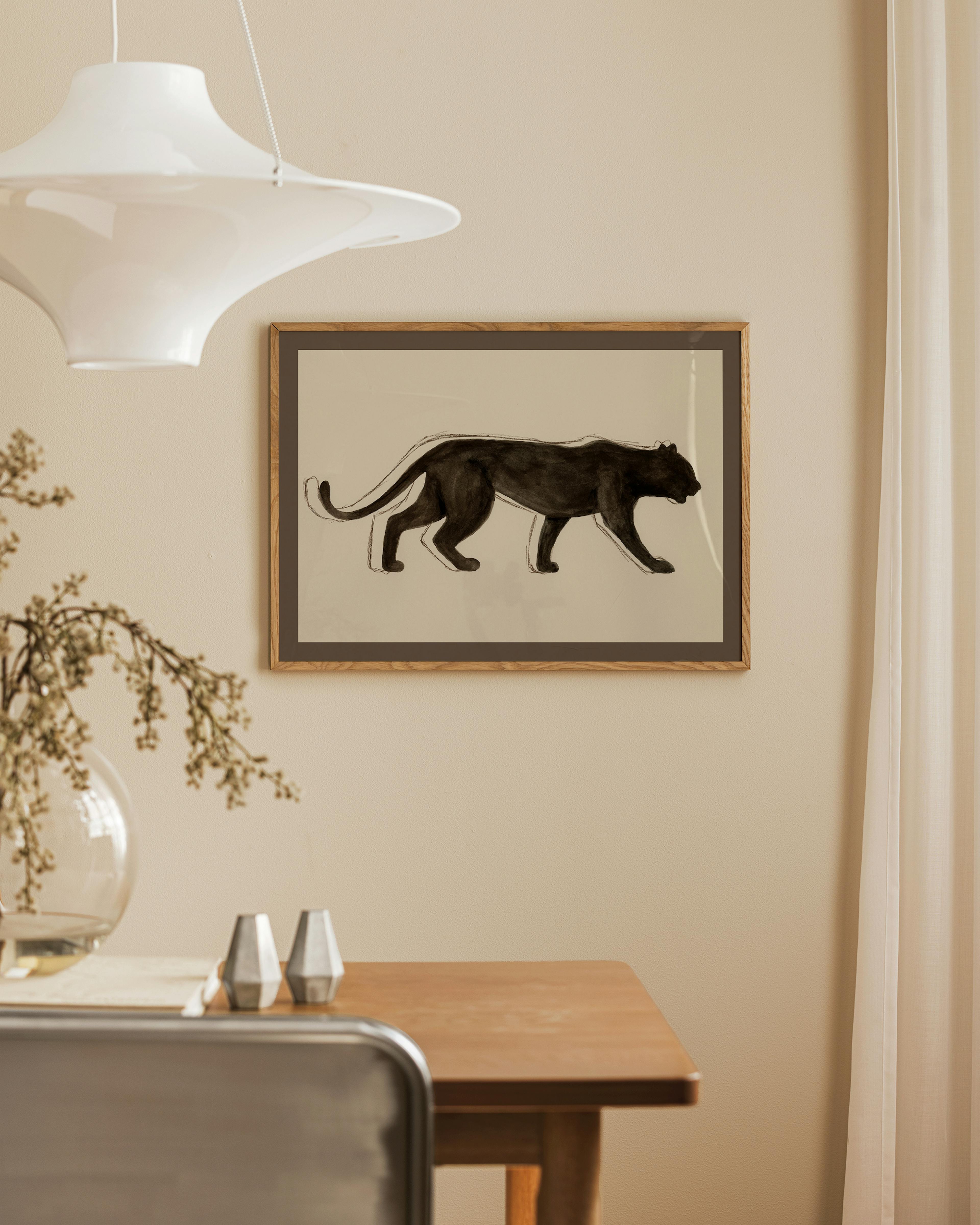 Black panther print with a white outline, hanging above a wooden dining table in a neutral room.