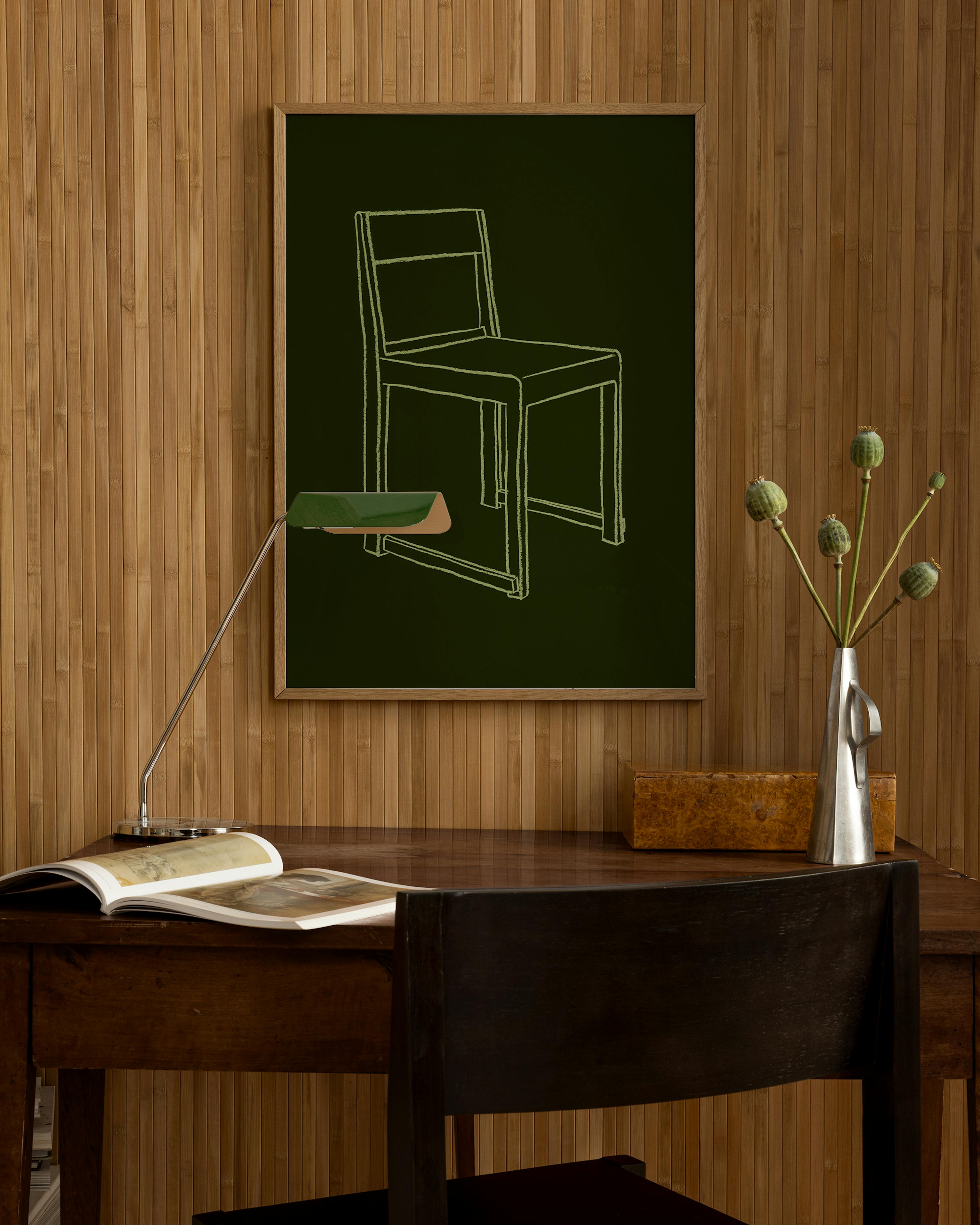 Póster de una silla dibujada con líneas blancas sobre un fondo verde oscuro, colgado en una pared de madera sobre un escritorio.