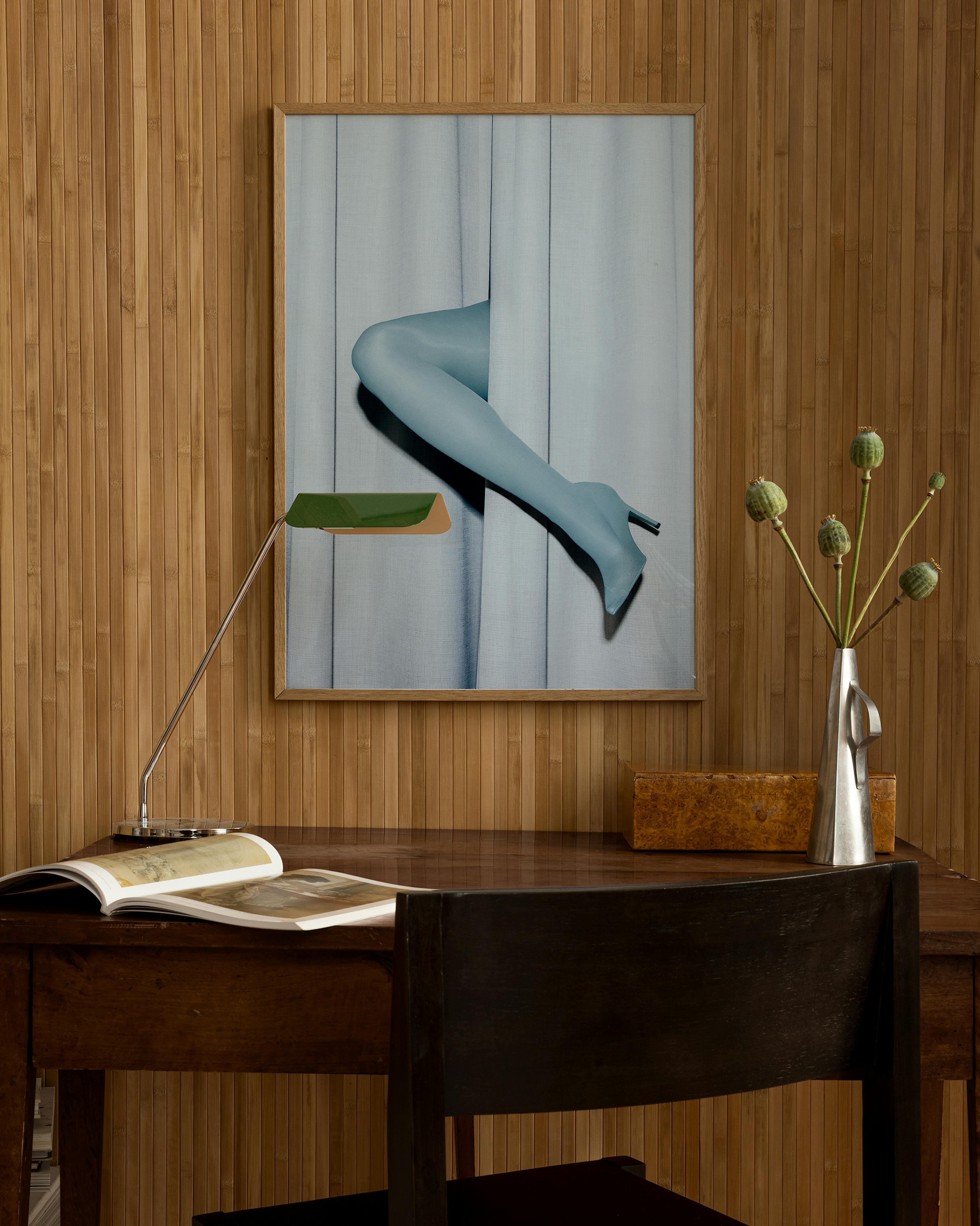Póster de piernas con medias azules y tacones, asomándose entre cortinas azules, colgado sobre un escritorio de madera.