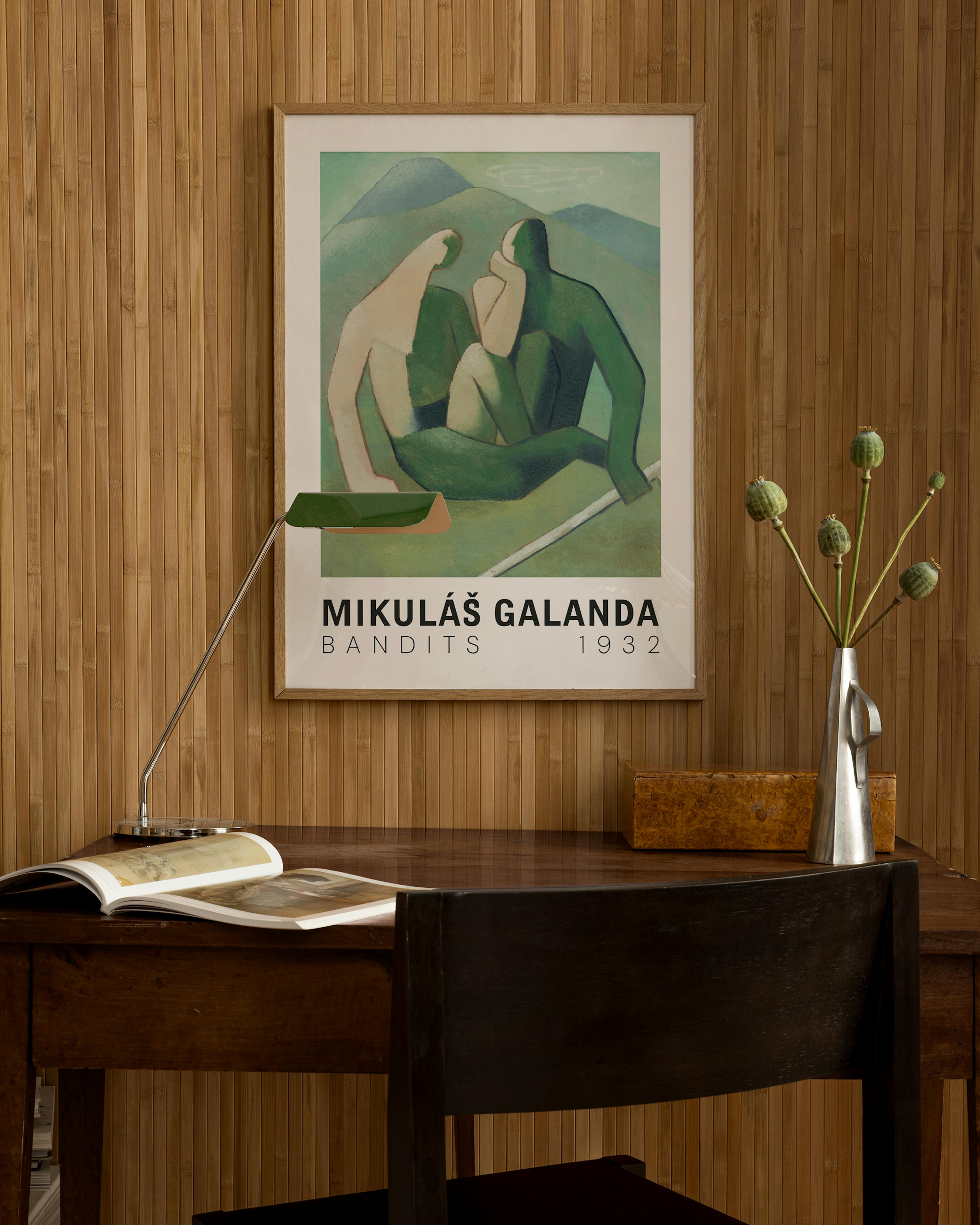 A Mikuláš Galanda Bandits print featuring two figures in green and beige, hanging above a wooden desk with a lamp and vase.