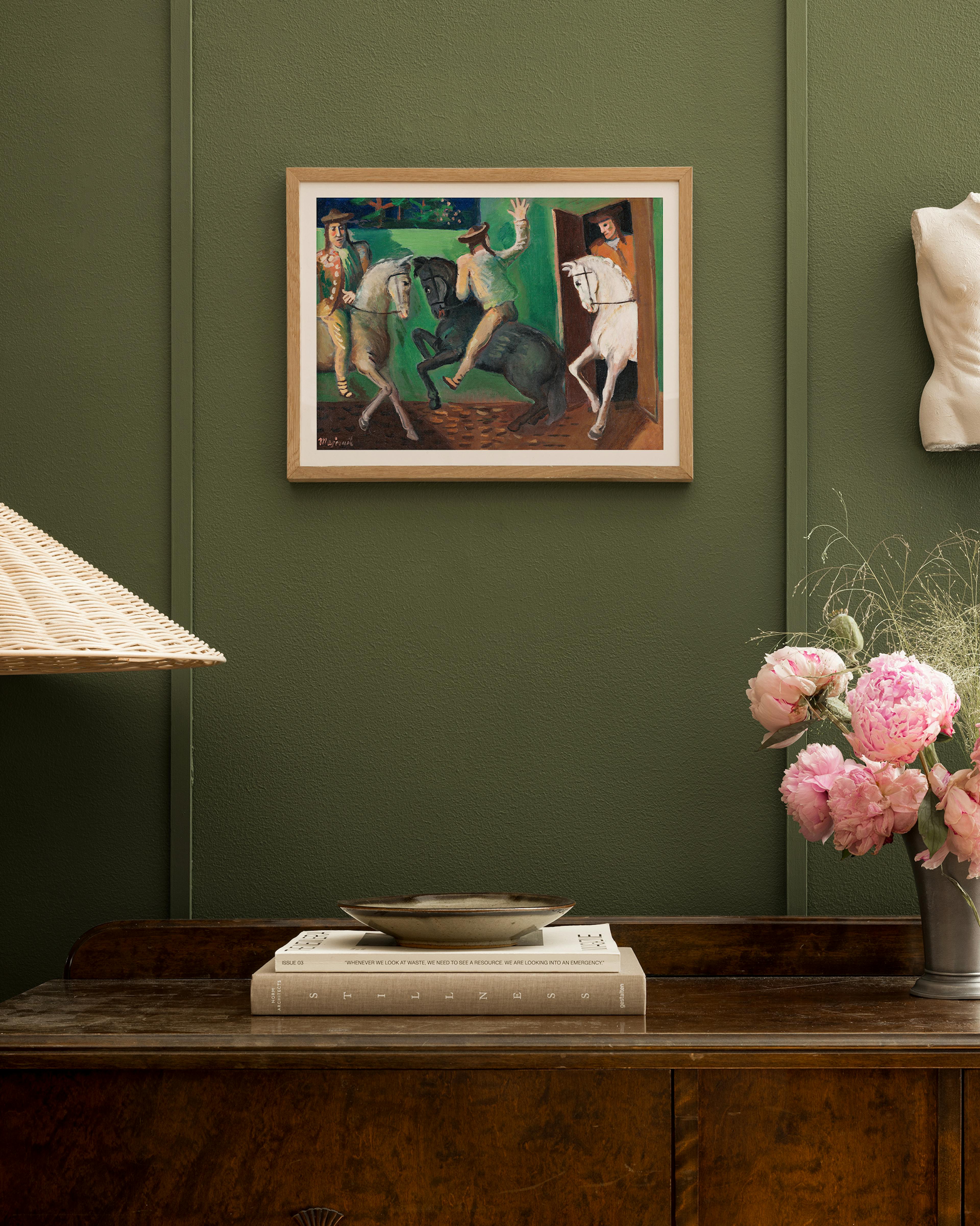 A print of three men on horses, one entering through a doorway, hanging above a wooden dresser with books and pink flowers.