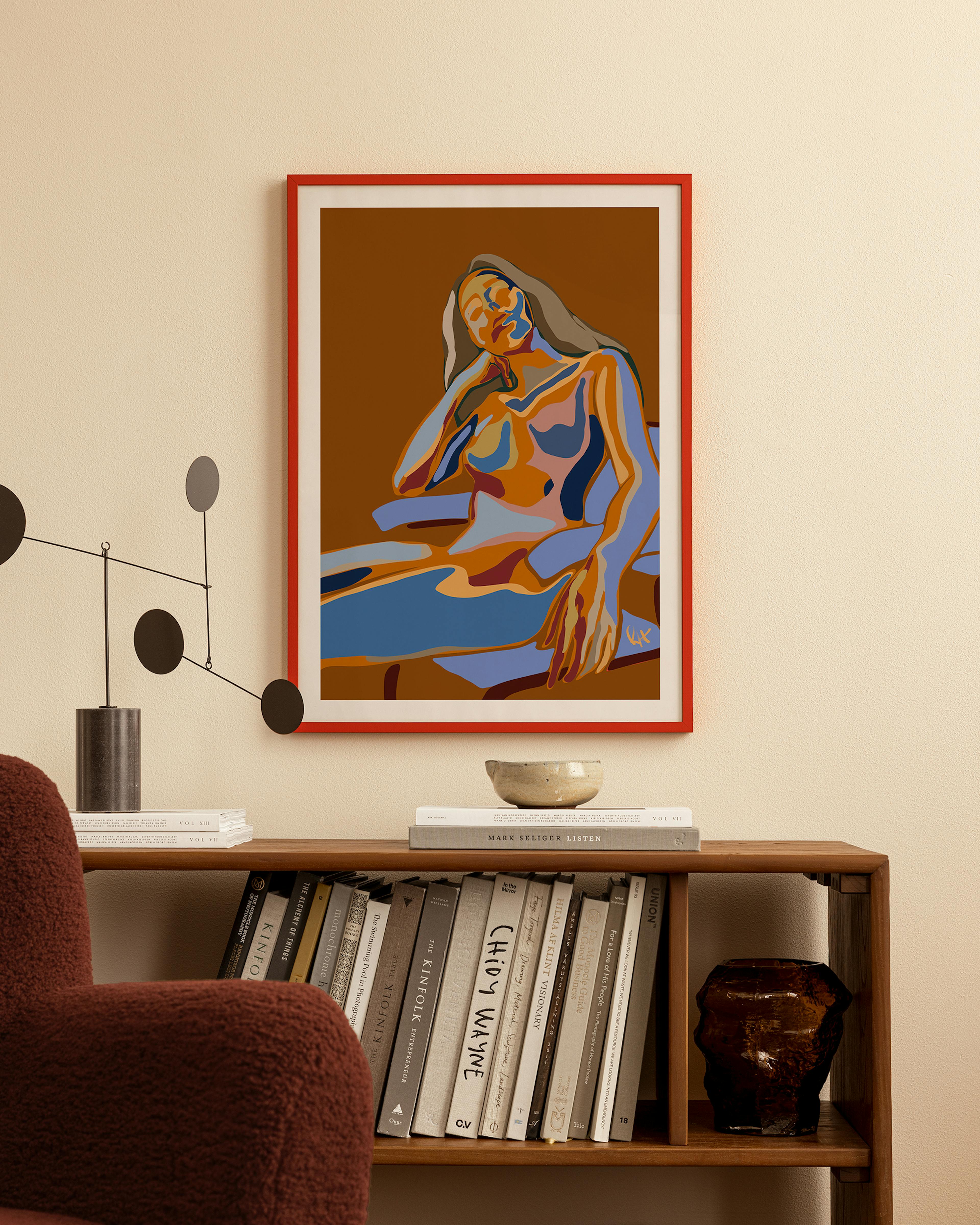 A colorful print of a reclining woman with long hair, in shades of brown, orange, and blue, displayed above a wooden bookshelf i