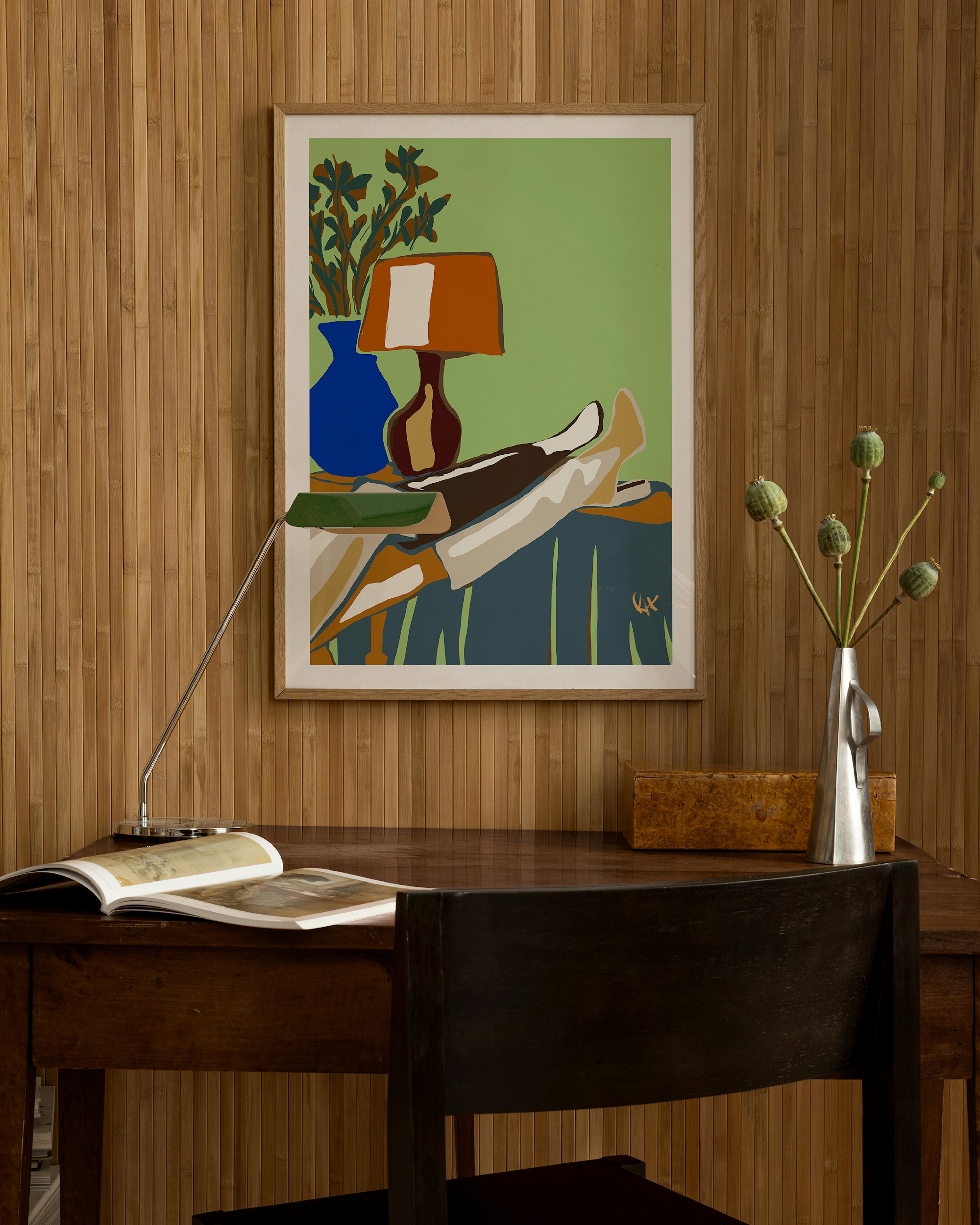Poster of a person relaxing with feet up, a blue vase, and an orange lamp, hanging above a wooden desk.