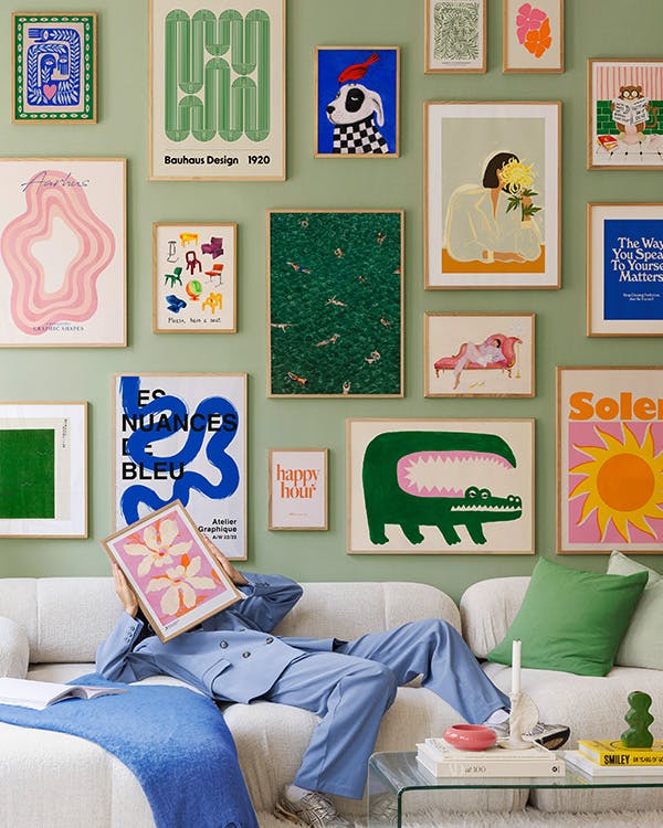 Een galeriewand met diverse opvallende prints, zoals een groene krokodil, zwemmende mensen en abstracte vormen, op een groene mu